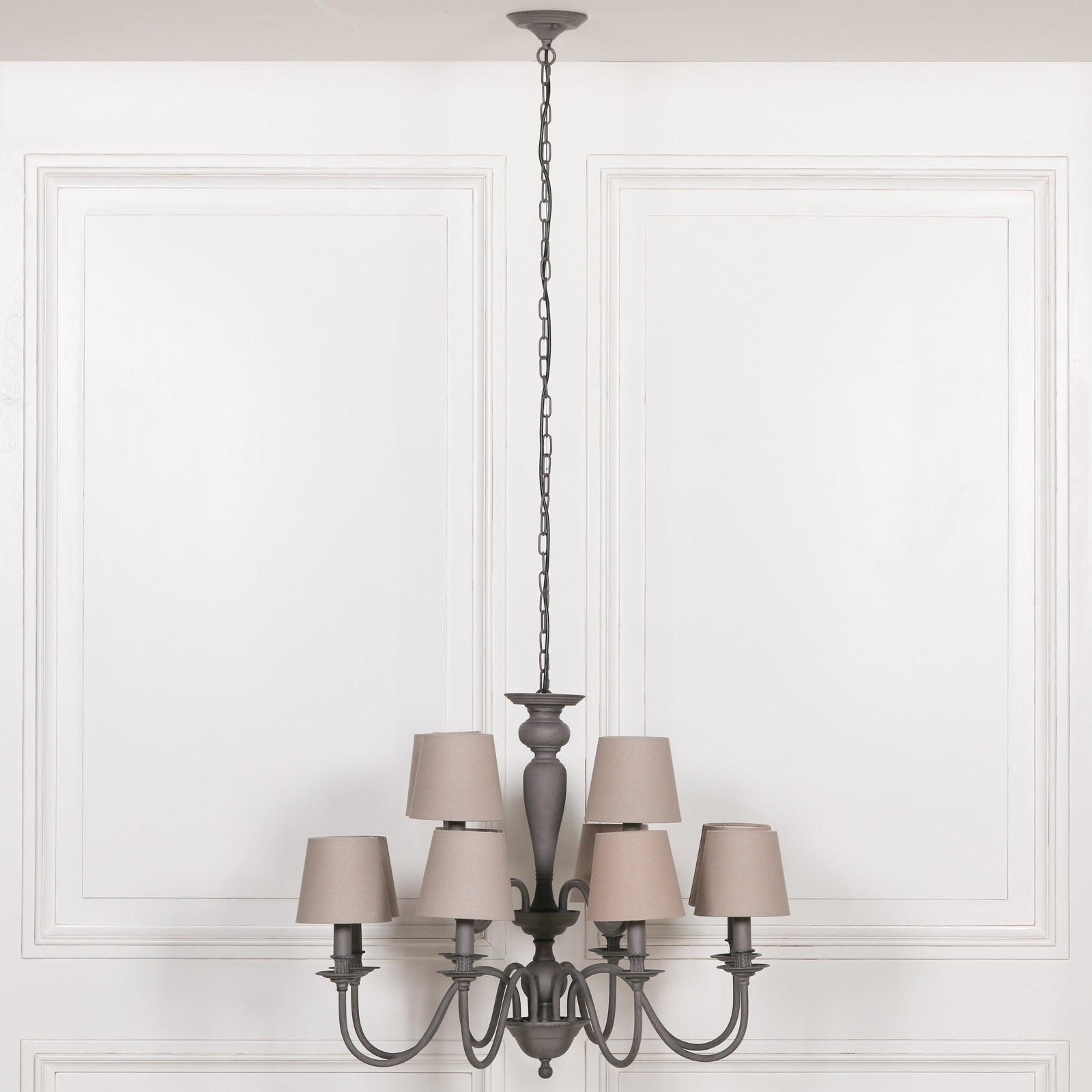 Evrard 86cm grey 12 light metal chandelier with taupe fabric shades against a white panelled wall.