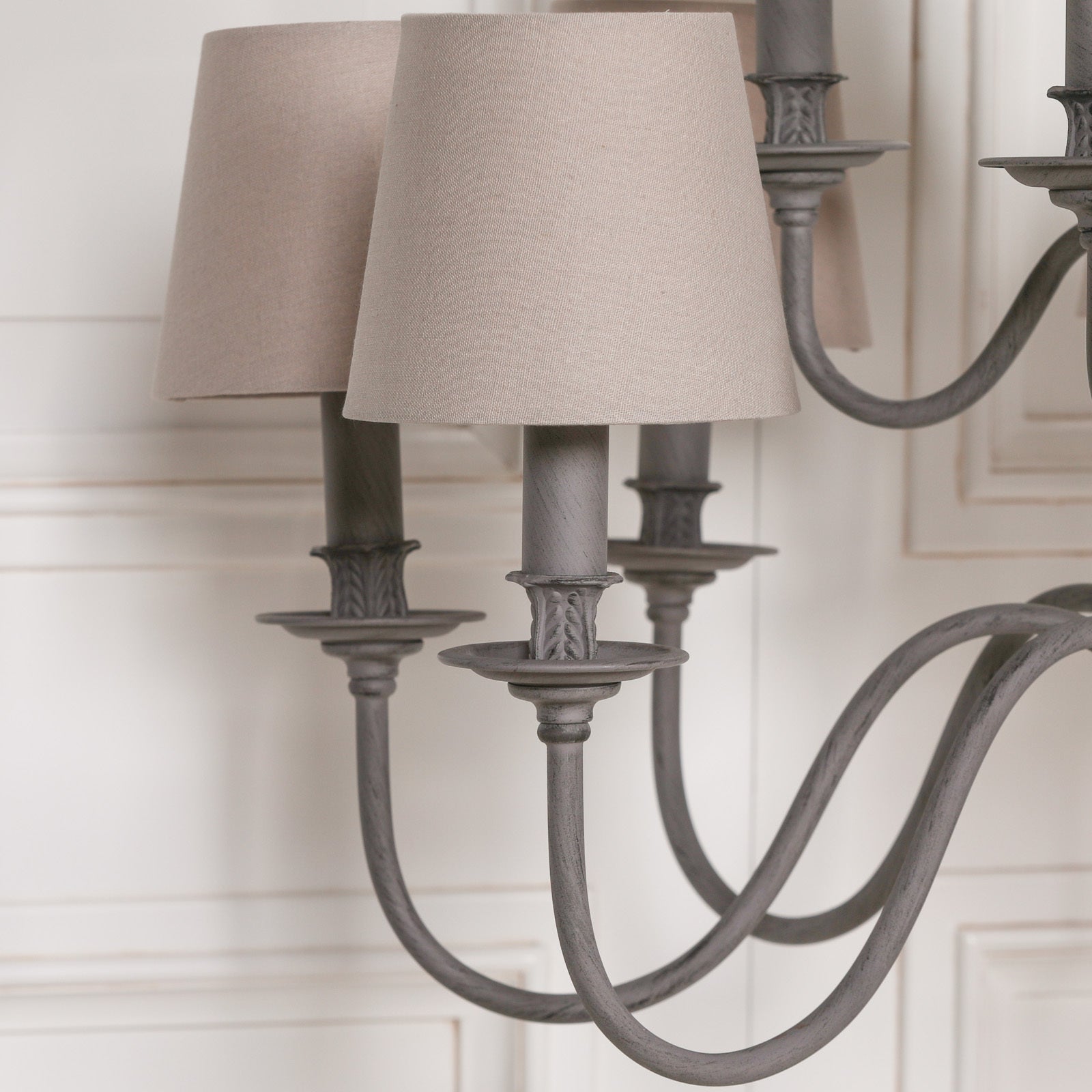 Close-up of Evrard chandelier curved grey metal arms and taupe fabric shades against a white panelled wall.
