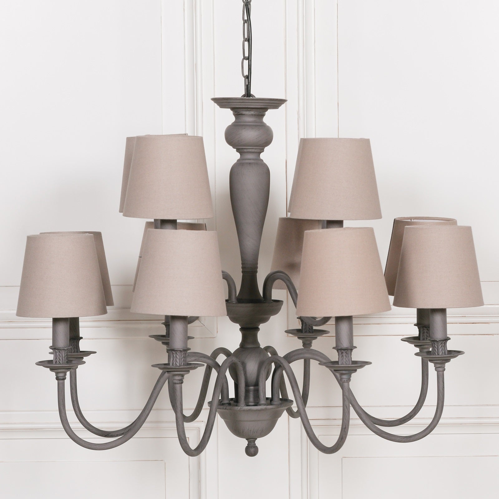 Grey 12 light chandelier with curved metal arms and taupe fabric shades against a white panelled background.