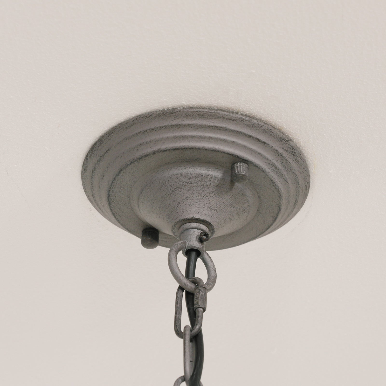 Close-up of Evrard grey chandelier ceiling canopy and hanging chain against an off-white ceiling.