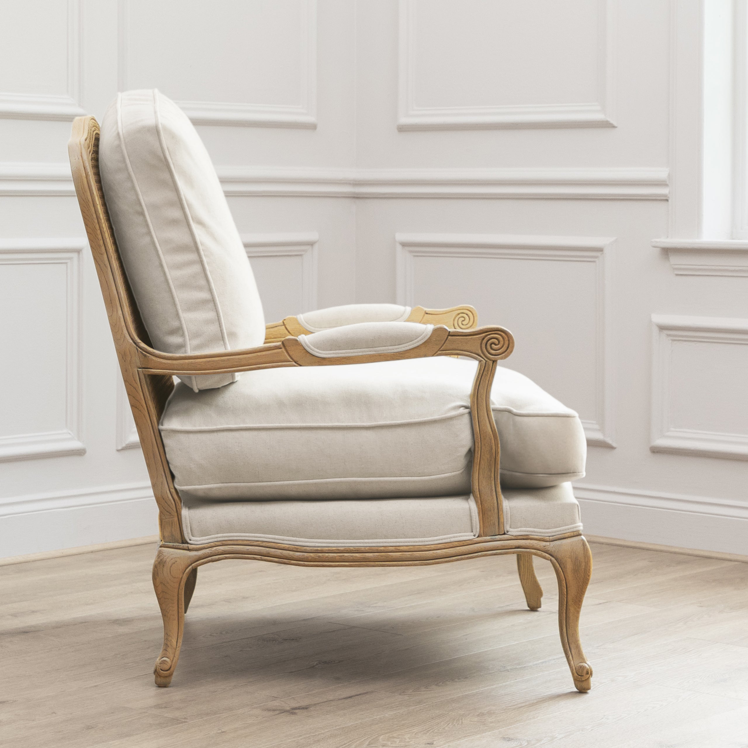Side view of Florence cream upholstered oak accent chair against white panelled walls and light wood flooring.