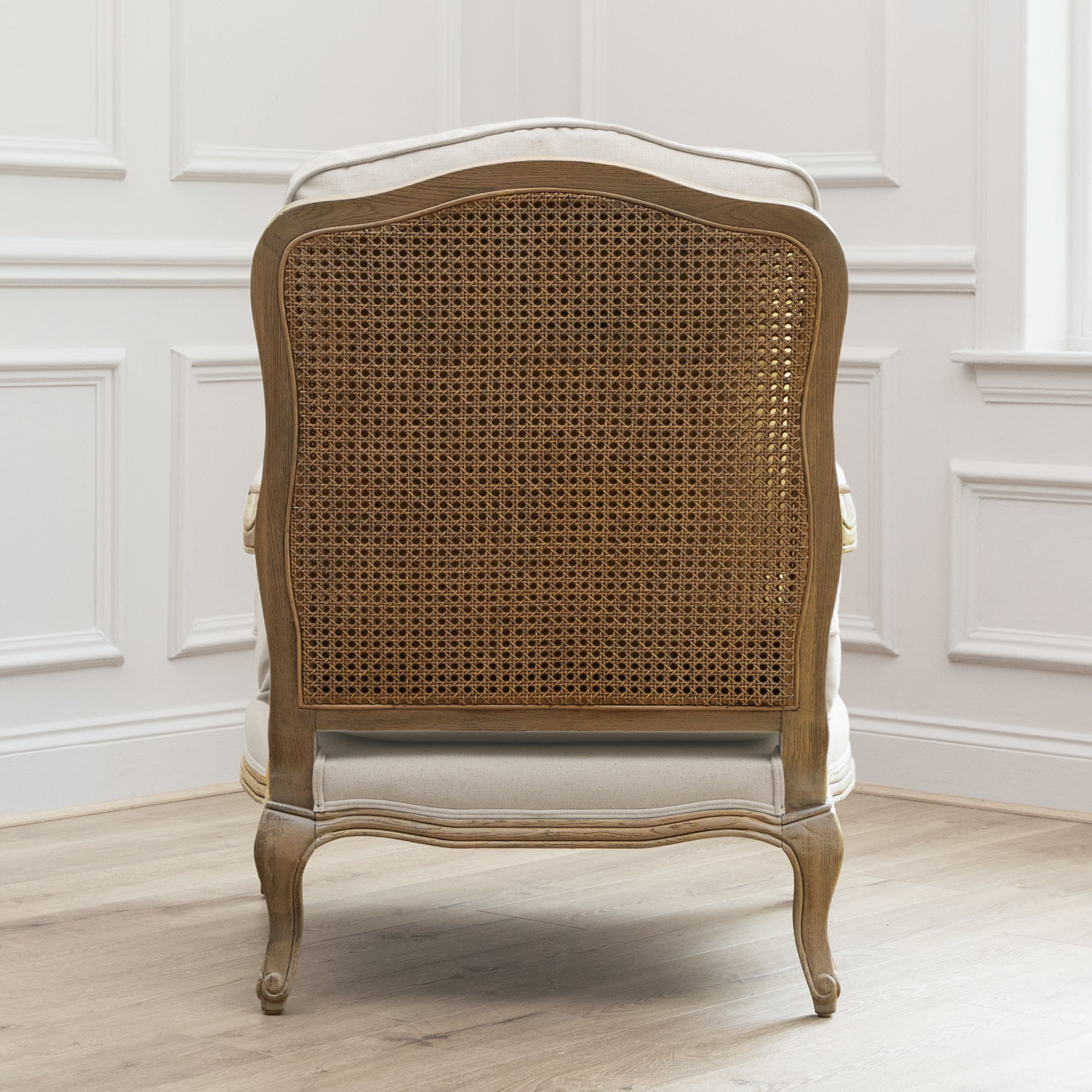 Rear view of Florence oak accent chair with cane back against white panelled walls and light wood flooring.