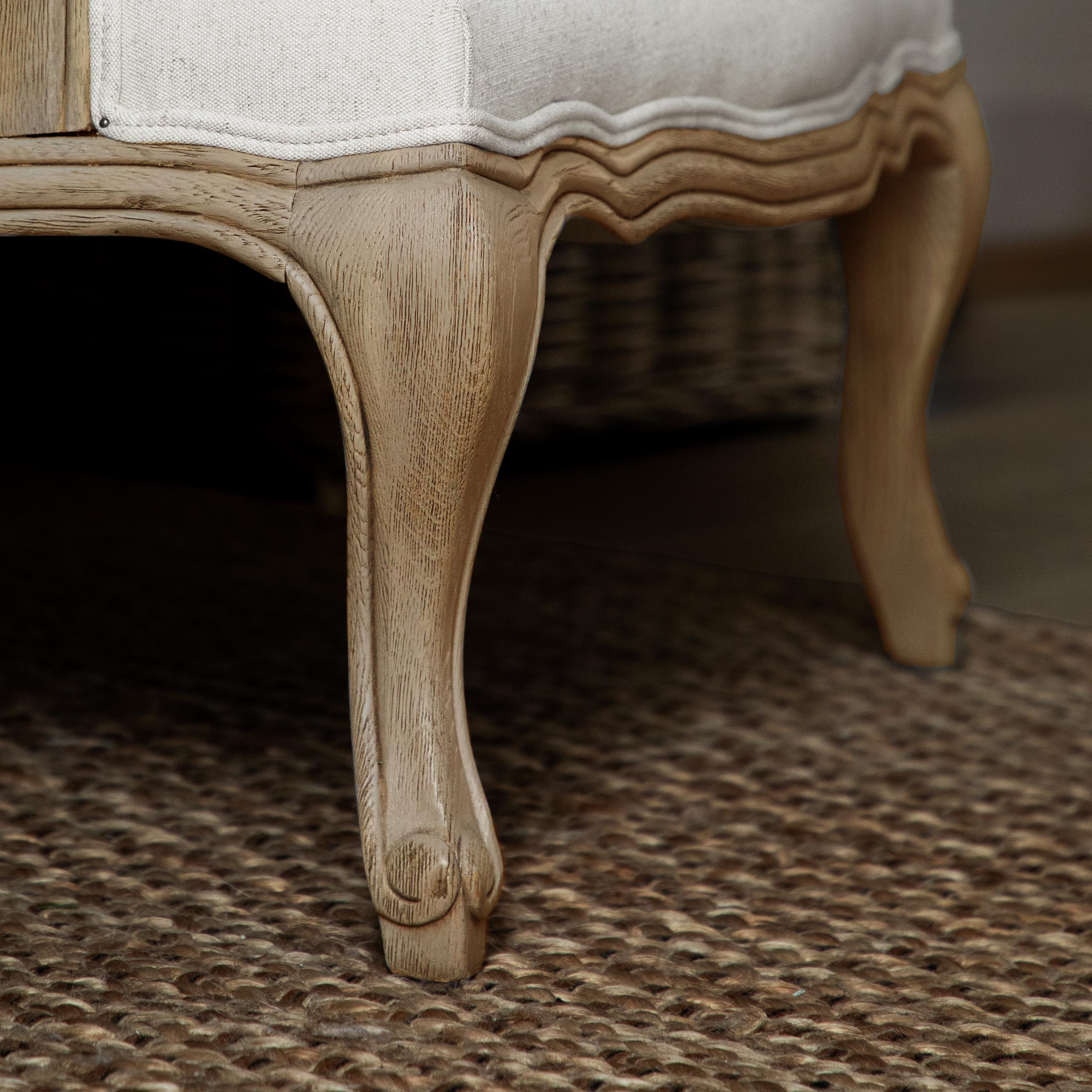 Close-up of Florence oak accent chair carved leg and cream upholstery on a textured brown rug.