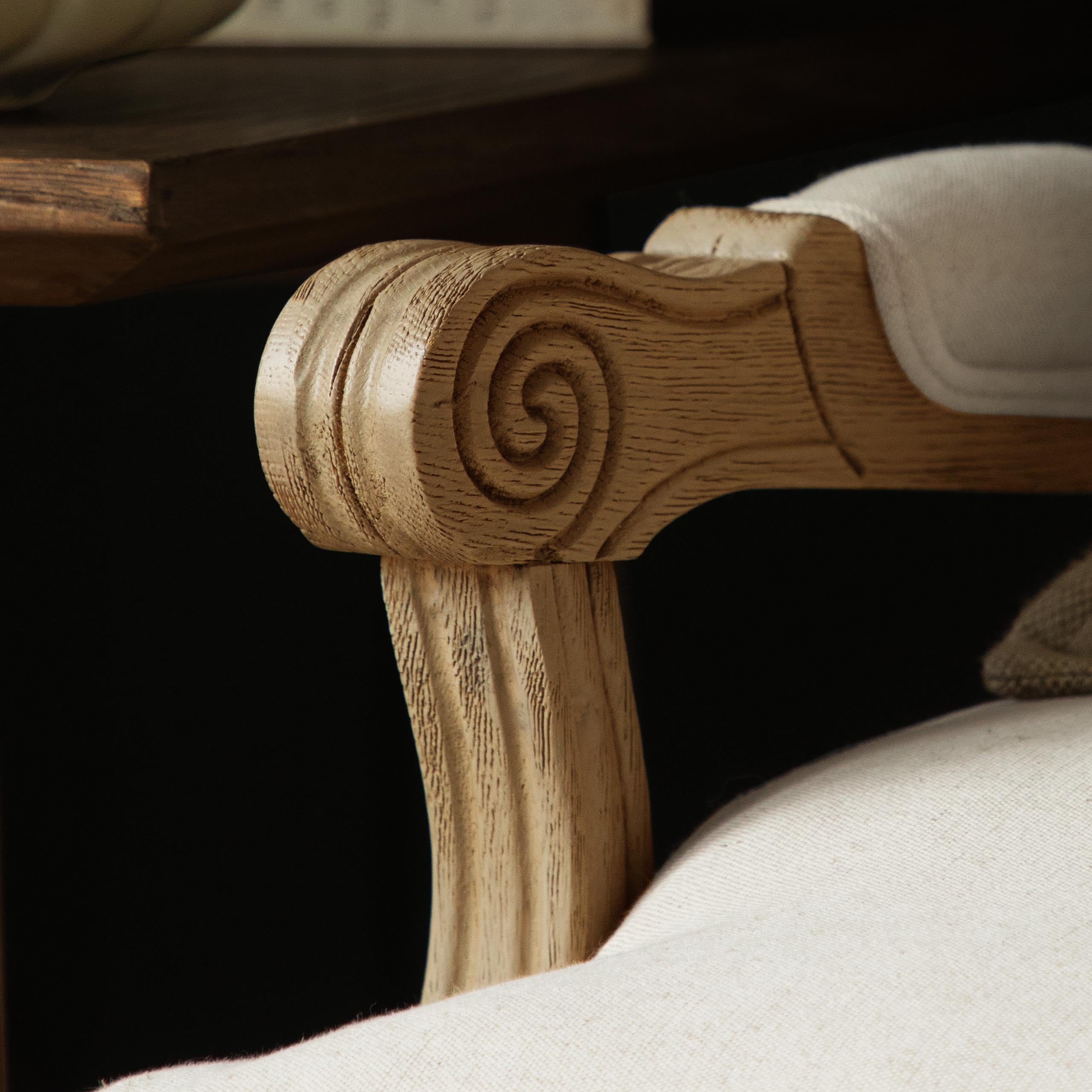 Close-up of Florence oak accent chair carved scroll arm and cream upholstery against a dark background.