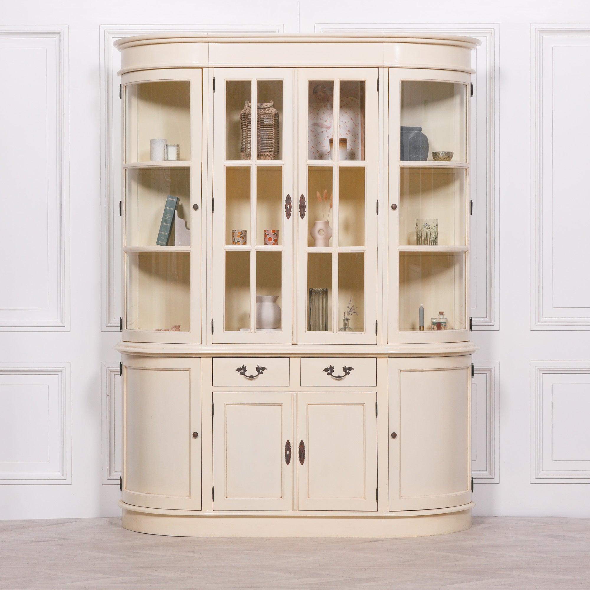 Geneviève aged cream mahogany display cabinet with styled glass shelves against a white panelled wall.