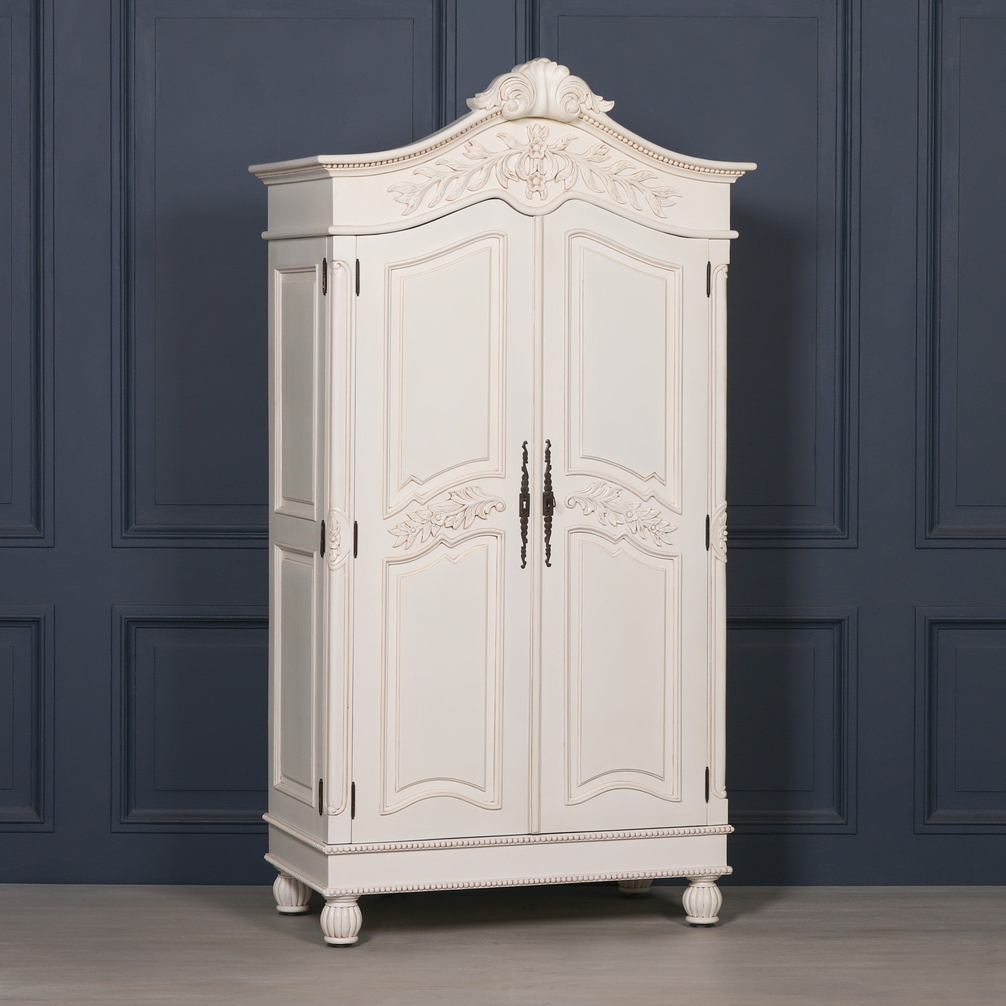 Angled view of the Geneviève Hand-Carved French Chateau Double Door Armoire Wardrobe in White Mahogany showcasing hand-carved floral detailing, decorative cornice, antique-inspired hardware and classic French bedroom furniture design.
