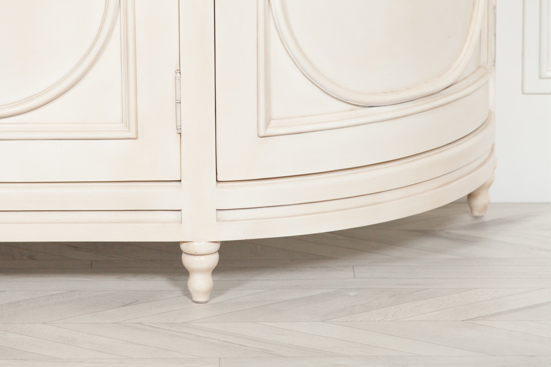Close-up detail of the Geneviève Large Aged Ivory Sideboard highlighting the elegant curved end panel, carved circular moulding, aged ivory finish, turned feet and handcrafted traditional furniture styling.