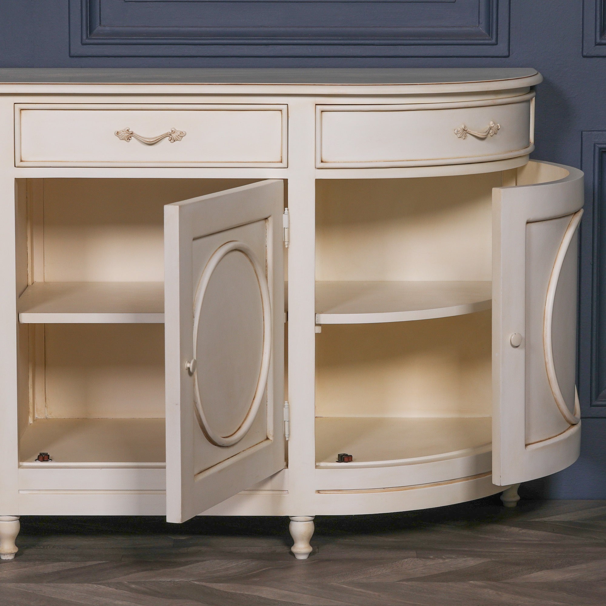 Close-up of the Geneviève Large Aged Ivory Sideboard with cabinet doors open, revealing spacious internal shelving, curved end compartments, four-door storage and aged ivory finish with ornate detailing.