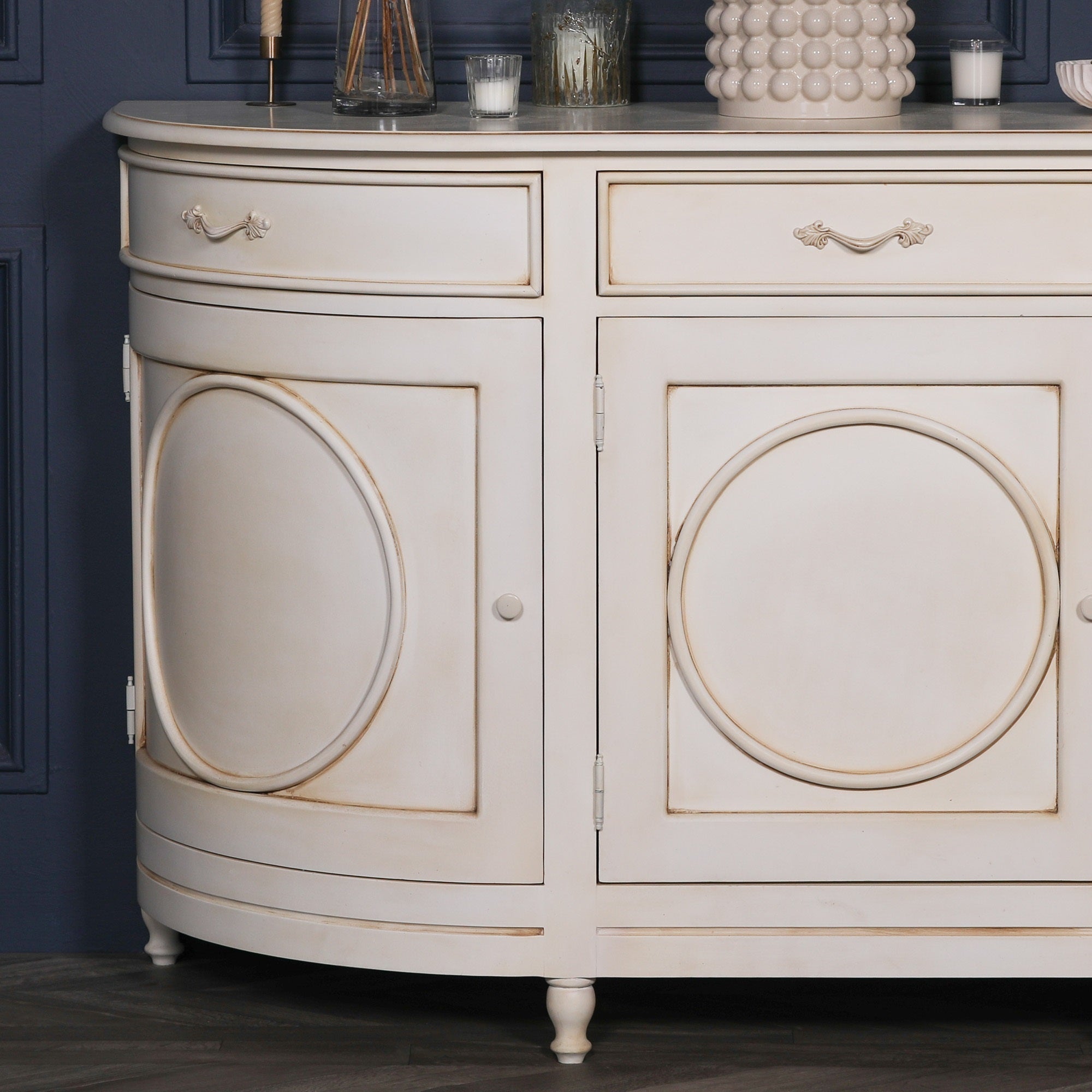 Close-up of the Geneviève Large Aged Ivory Sideboard with 4 Doors, 4 Drawers & Ornate Detailing highlighting the carved circular door panel, aged ivory painted finish, antique-inspired craftsmanship and elegant curved cabinet design.