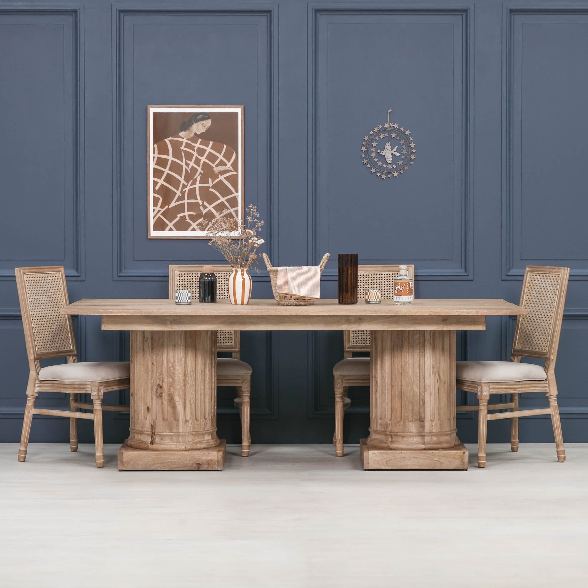 Henri 220cm Rustic Mango Wood Rectangular Column Dining Table styled with woven dining chairs in an elegant dining room, showcasing the solid mango wood construction, twin fluted column pedestal bases and spacious rectangular tabletop that comfortably seats 8 to 10 people.