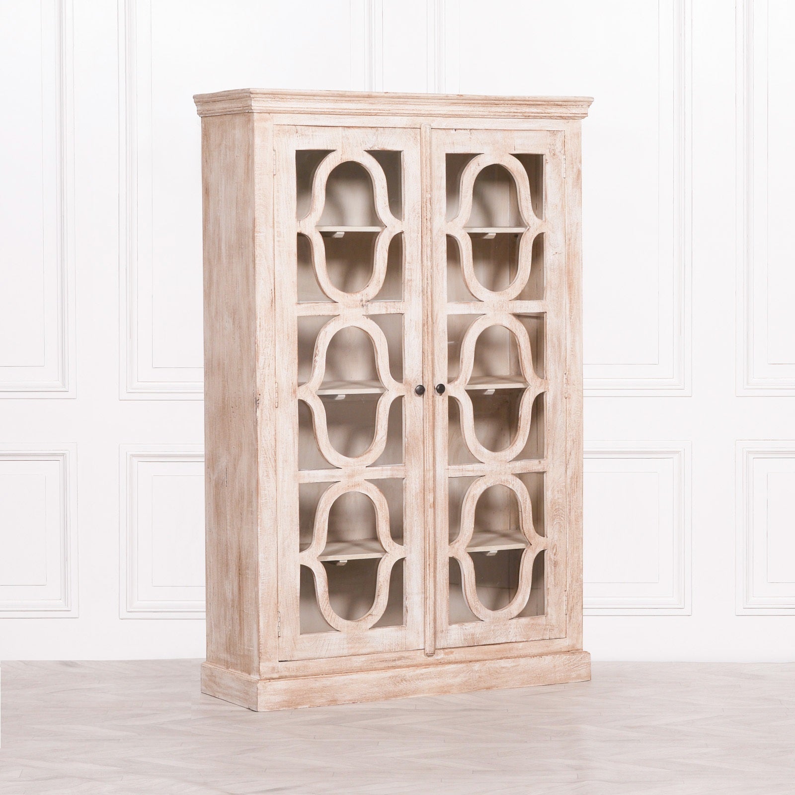 Angled front view of the Henri Rustic Mango Wood Display Cabinet with 2 doors, showcasing ornate carved glass door detailing, spacious display shelving, handcrafted mango wood construction and a beautifully weathered rustic finish for traditional and farmhouse interiors.