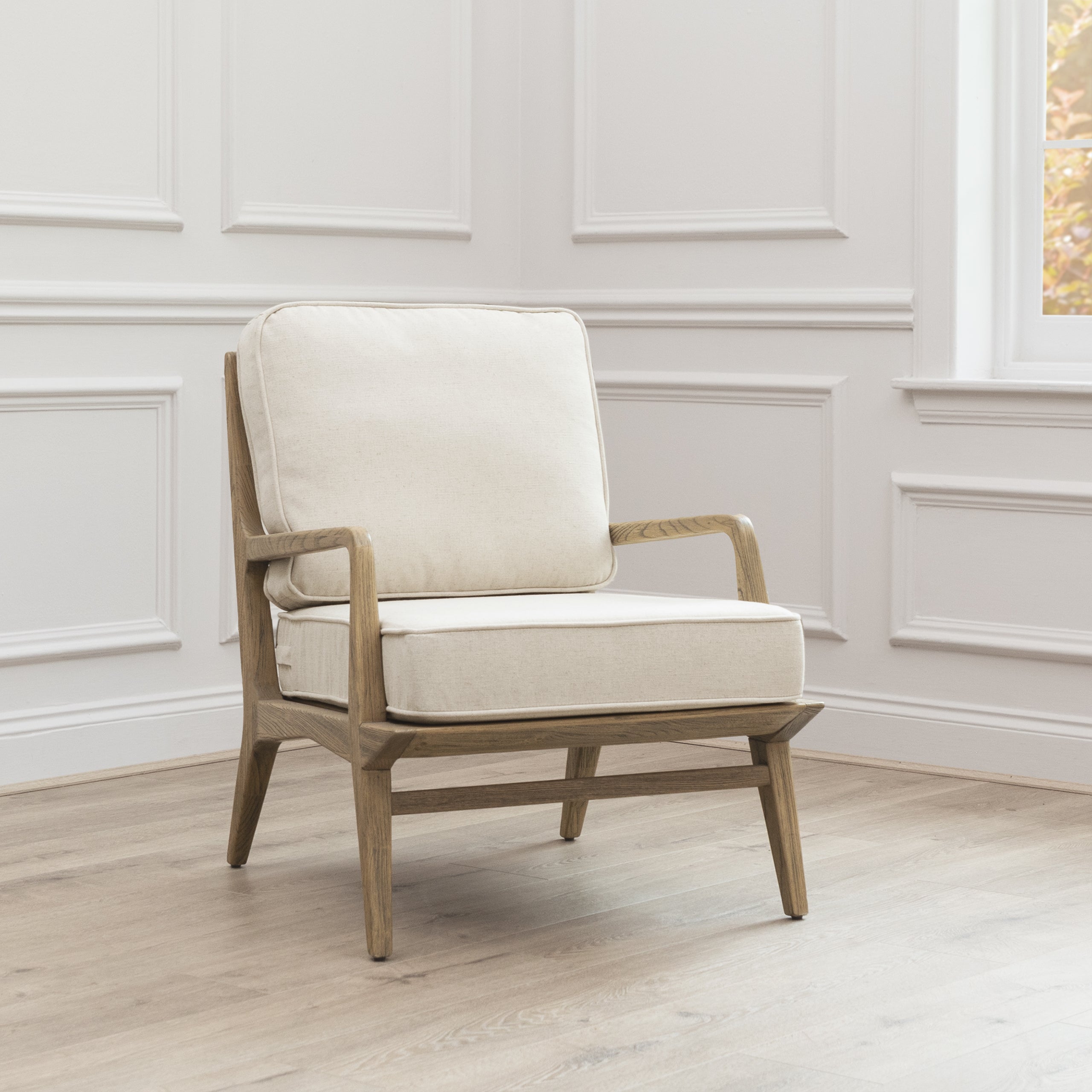 Angled view of Idris cream upholstered oak accent chair against white panelled walls and light wood flooring.
