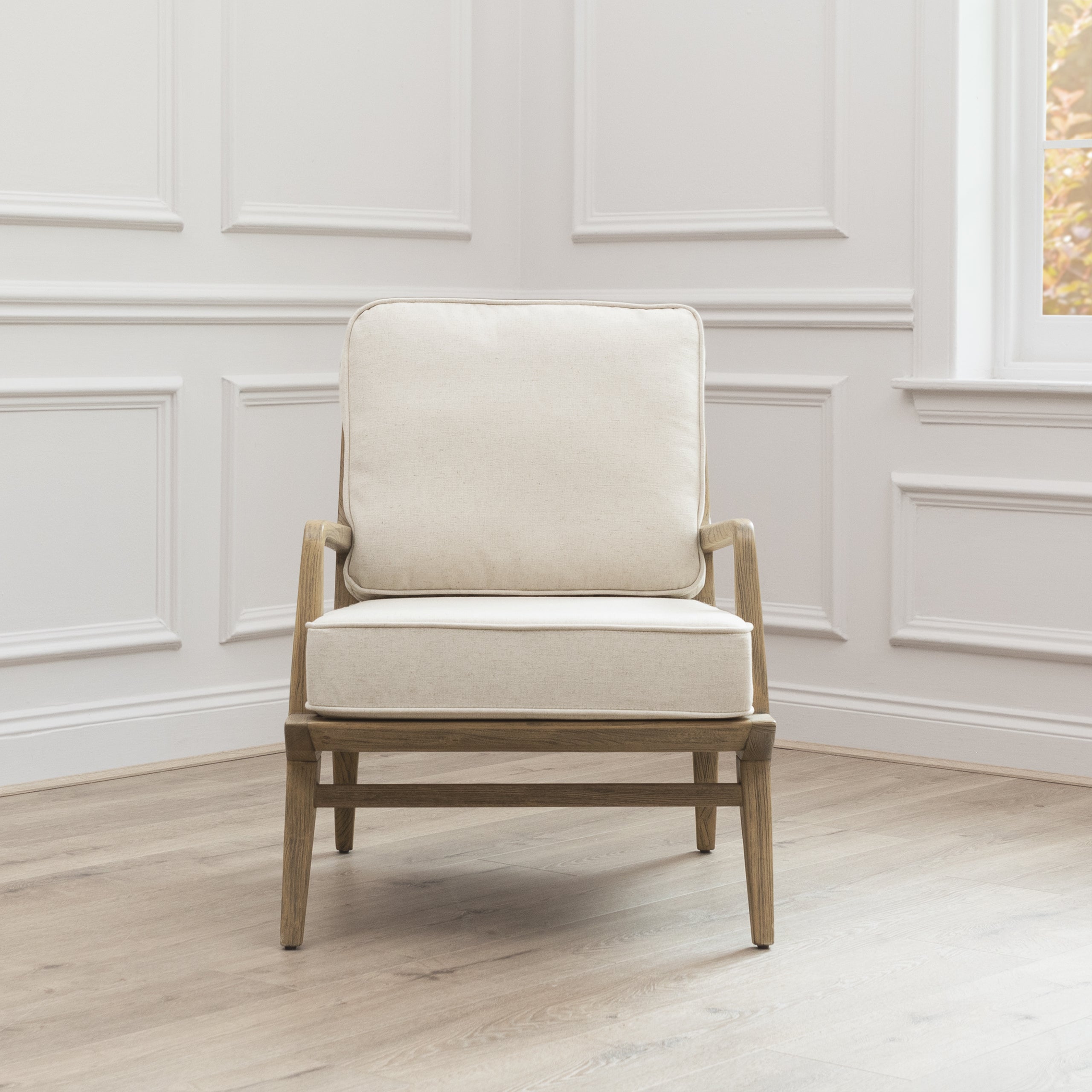 Front view of Idris cream upholstered oak accent chair against white panelled walls and light wood flooring.