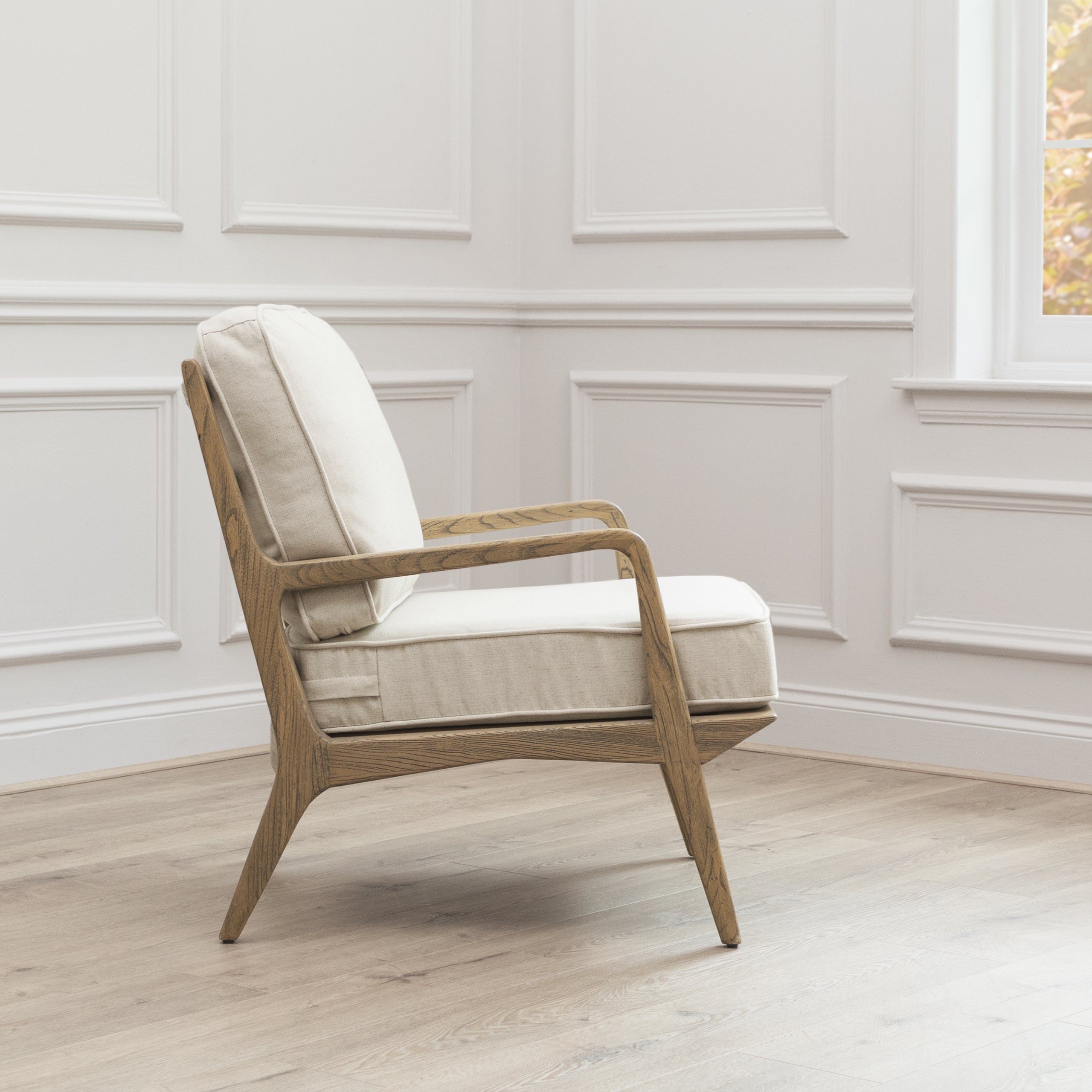 Side view of Idris cream upholstered oak accent chair against white panelled walls and light wood flooring.