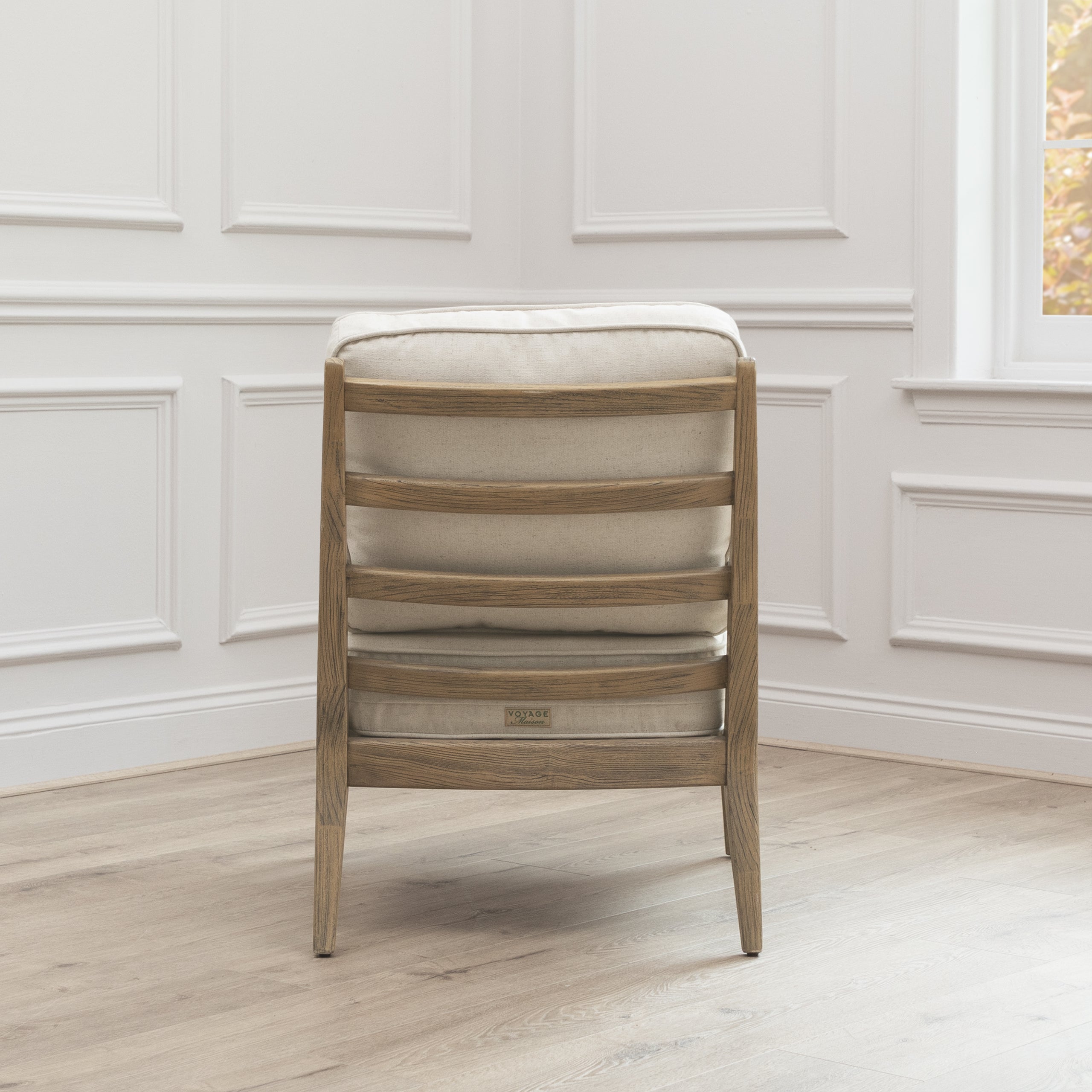 Rear view of Idris oak accent chair with cream upholstery against white panelled walls and light wood flooring.