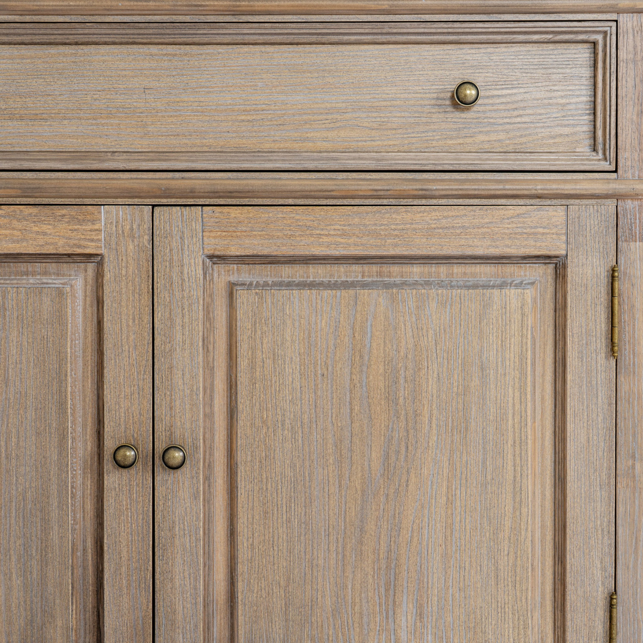 Close-up of Laurent brown wood display cabinet showing drawer, panelled doors and brass hardware on a white background.