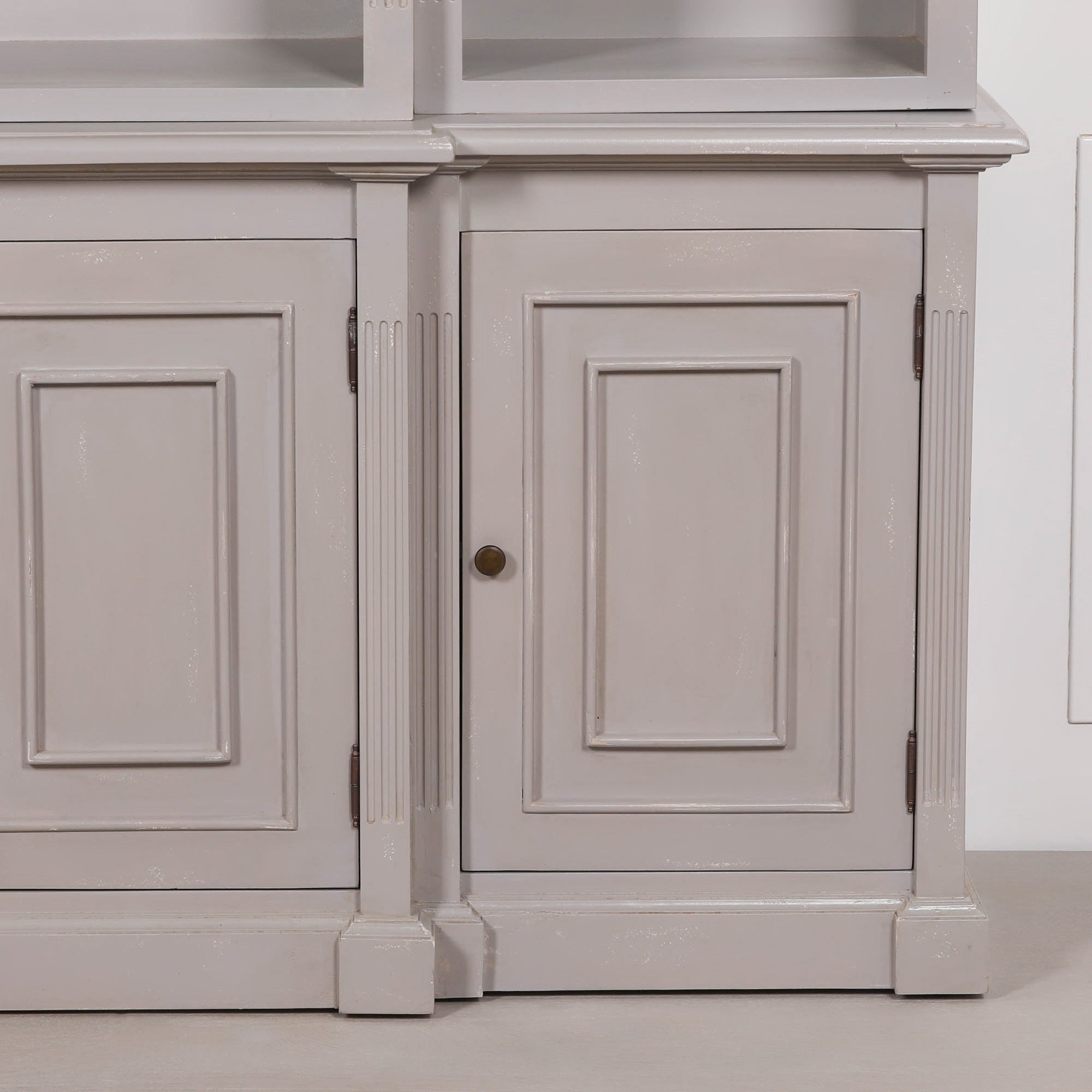 Close-up of Laurent distressed mahogany bookcase with panelled storage door and brass knob against a white background