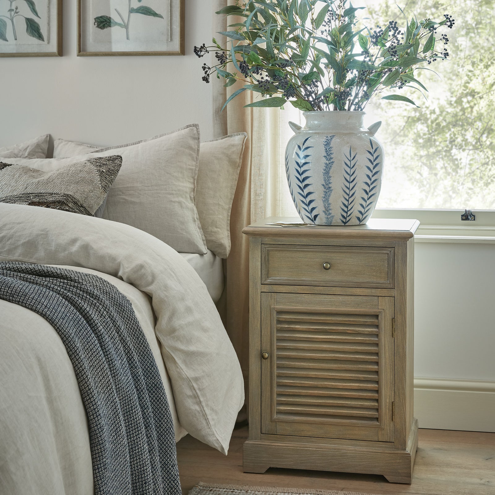 Laurent Wood Storage Chest with 1 Door & 1 Drawer – Right Hand styled as a bedside cabinet in a contemporary bedroom, featuring a natural wood finish, shutter-style door, spacious drawer and practical bedside storage beside a bed and window.