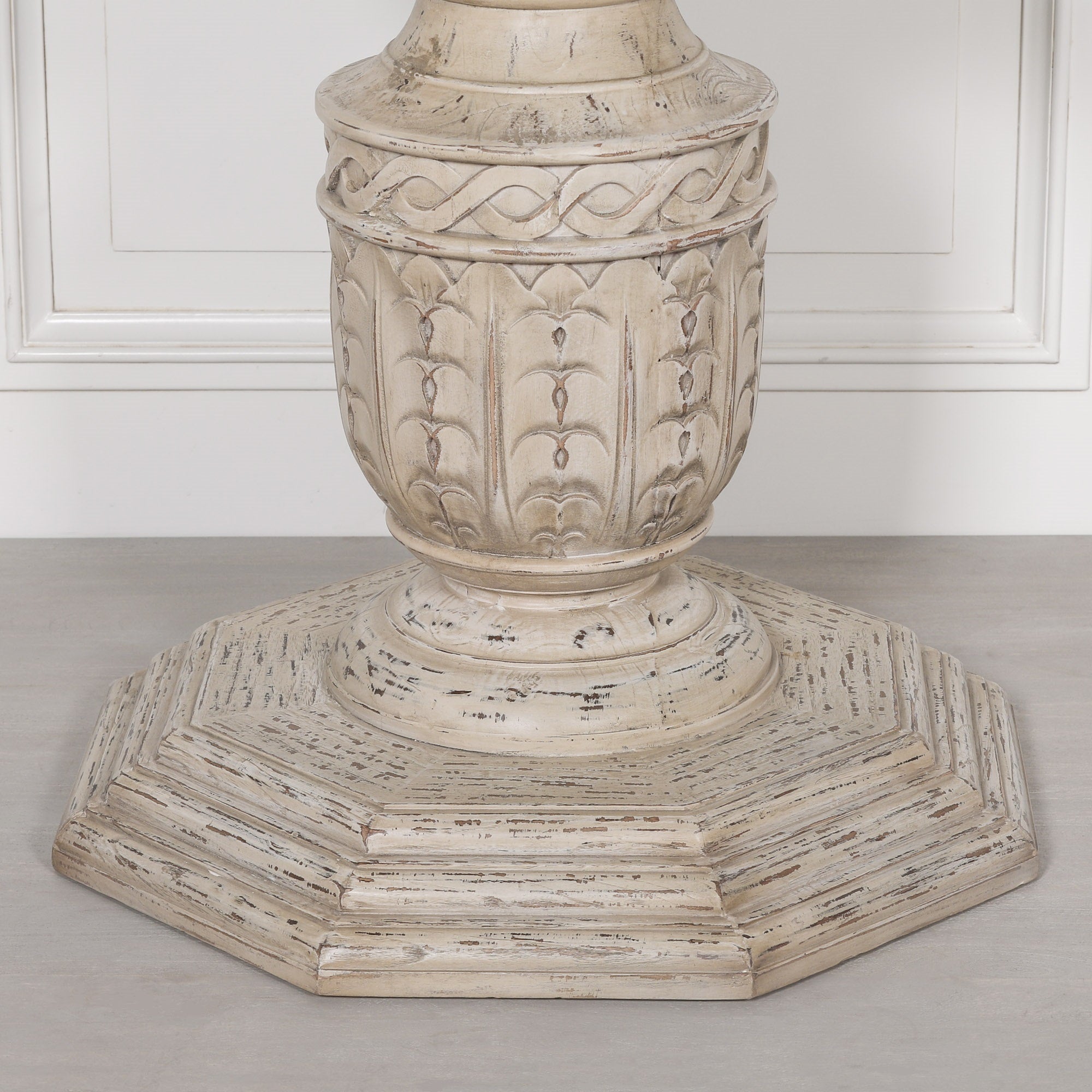 Close-up of the Léandre Round Pedestal Dining Table 145cm showcasing the intricately hand-carved white cedar pedestal base, distressed artisan finish and decorative octagonal plinth with traditional carved detailing.