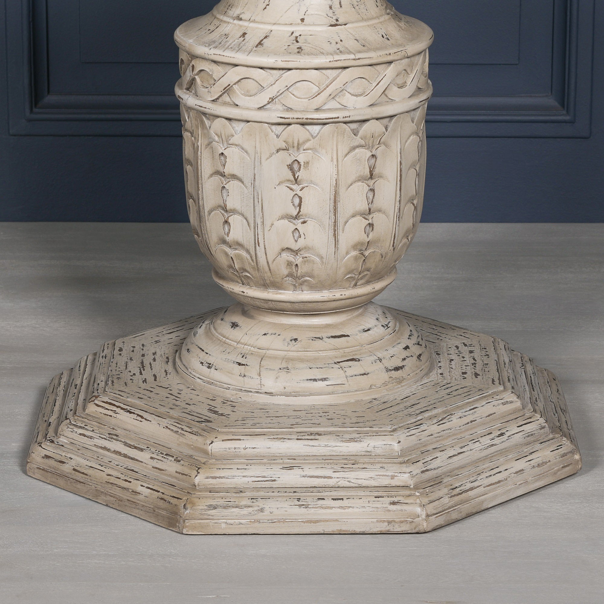 Detailed close-up of the Léandre Round Pedestal Dining Table 145cm showing the ornate hexagonal sculptural hand-carved white cedar pedestal, distressed artisan finish, carved decorative motifs and substantial octagonal base.
