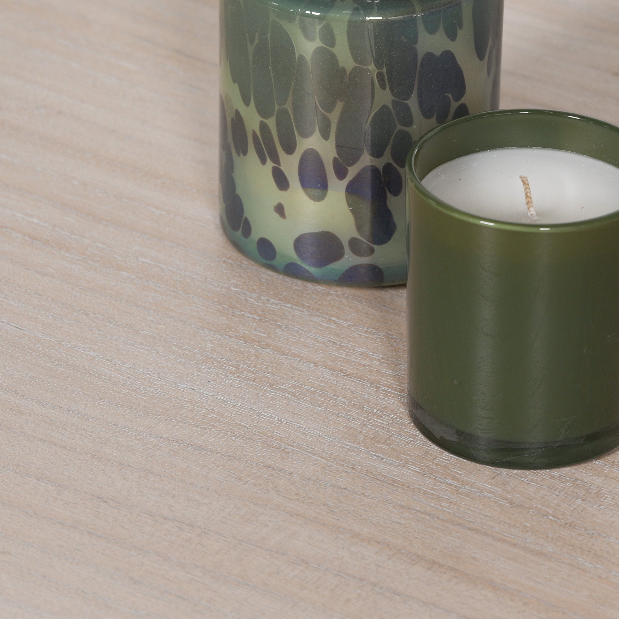 Close-up of the Léandre Round Pedestal Dining Table 145cm highlighting the distressed white cedar wood tabletop, natural timber grain, softly weathered finish and gently rounded edge profile. featuring 2 green candles one with a leopard pattern.