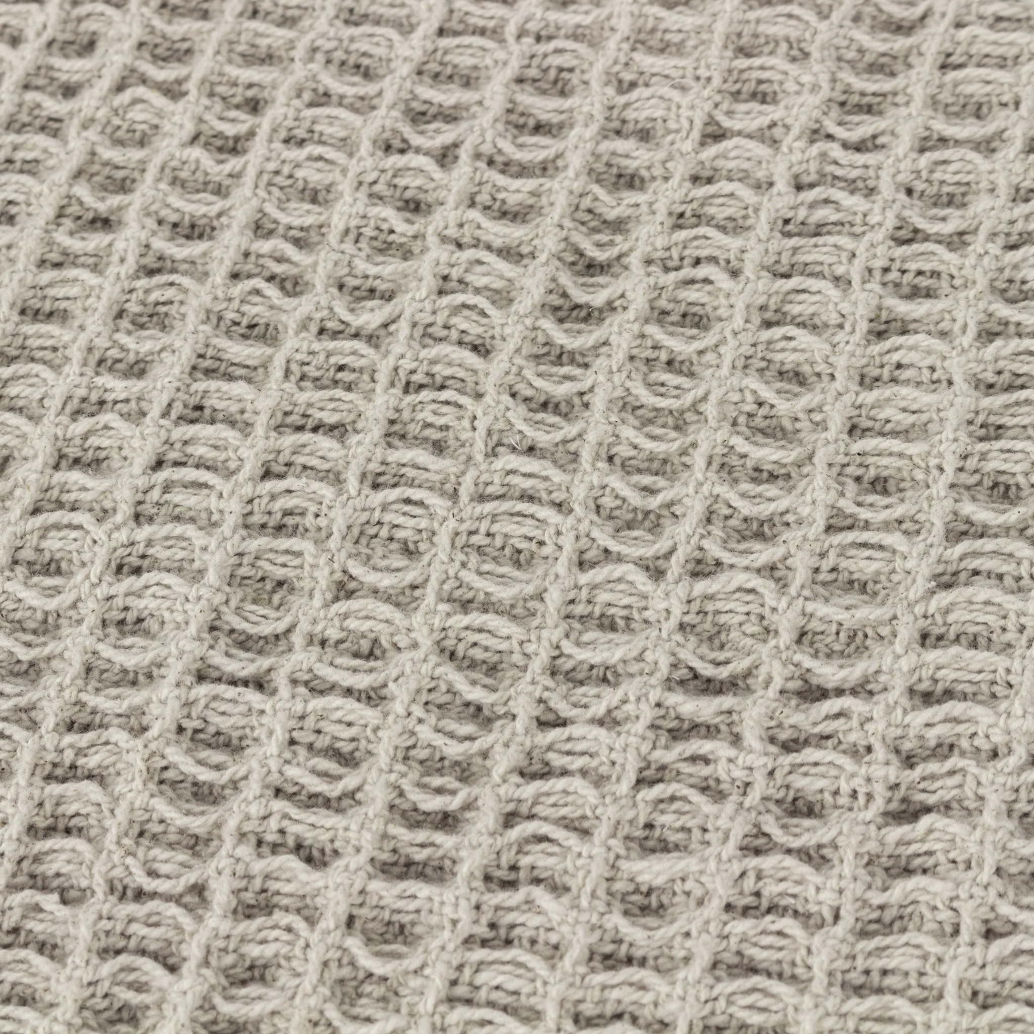 Close-up of Léna stone cotton throw showing the raised waffle weave texture on a neutral fabric background.