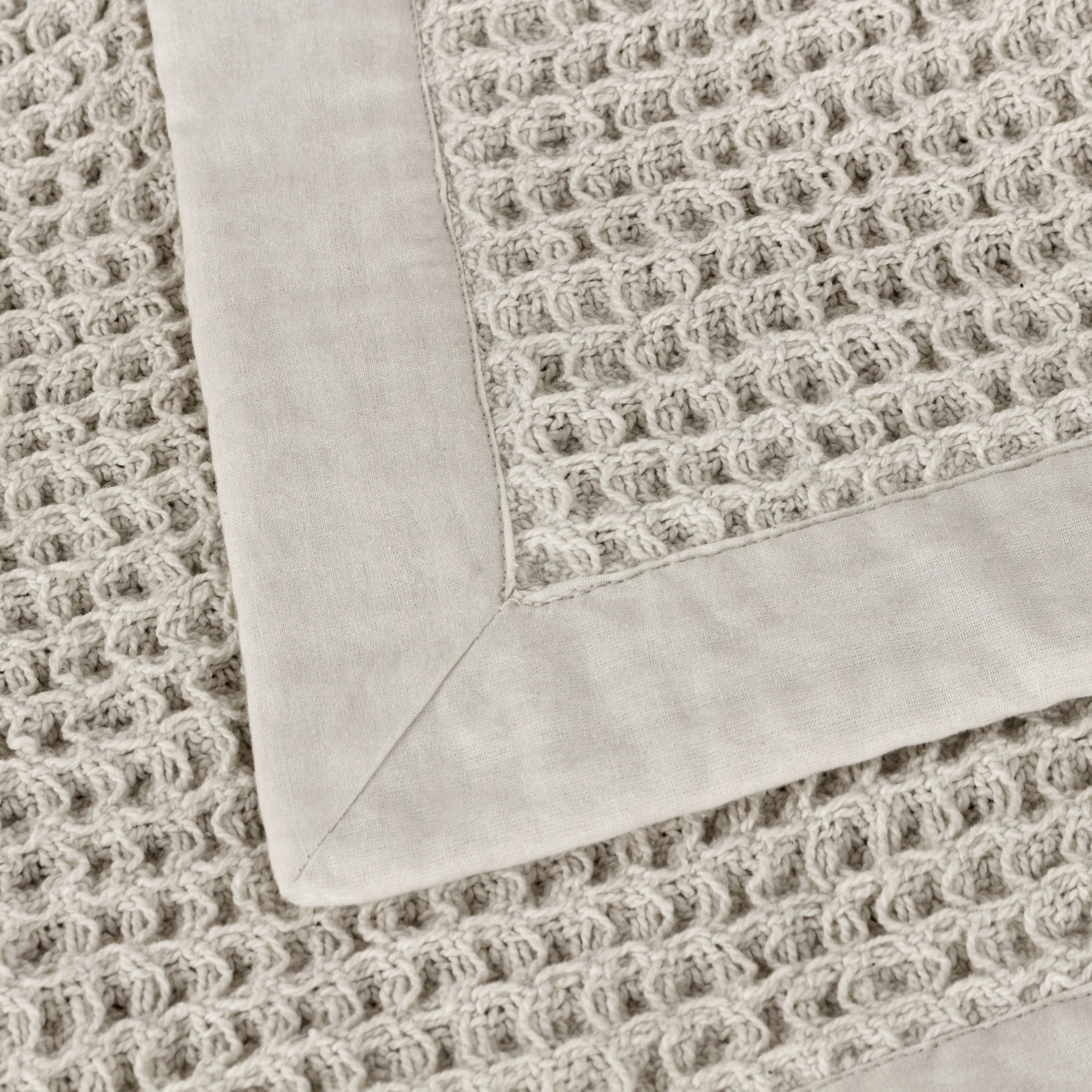 Close-up of Léna stone waffle cotton throw showing its smooth natural border and textured weave on a white background.