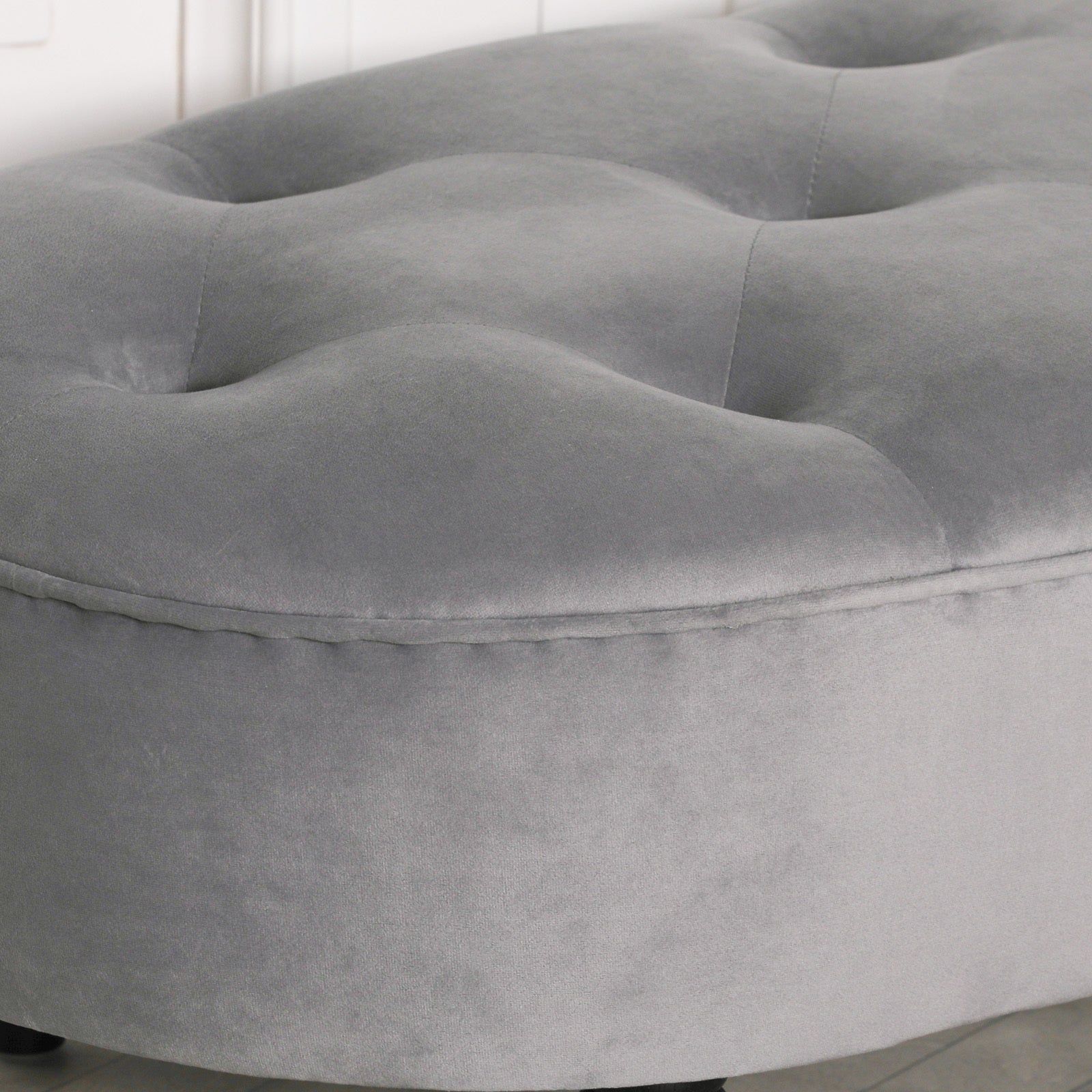 Close-up of grey velvet bench tufting and piped upholstery against a white panelled wall and pale wood floor.