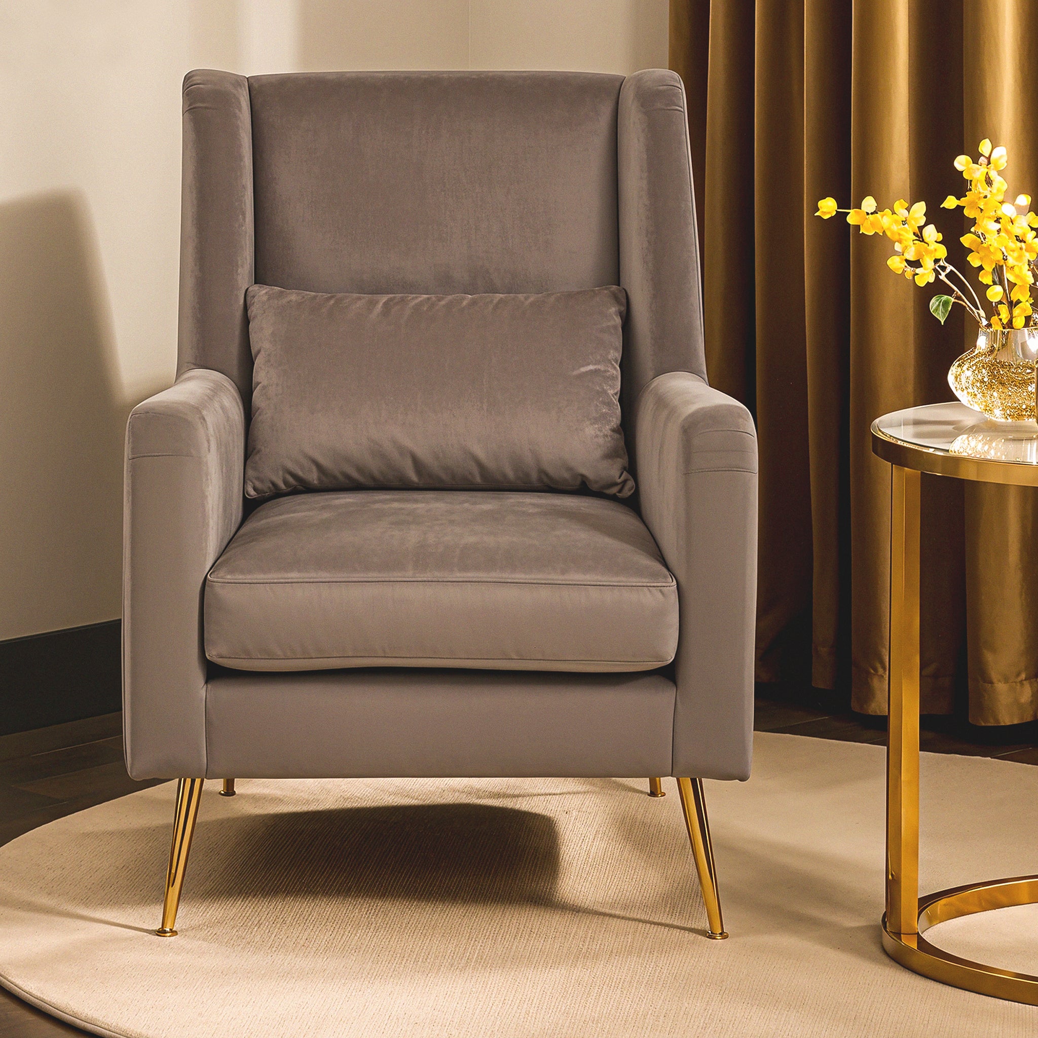 Lucien Grey Velvet High-Back Accent Chair with Angular Gold Legs styled in a contemporary living room beside a gold side table, showcasing luxurious grey velvet upholstery, supportive high back, matching lumbar cushion and elegant angular gold legs.