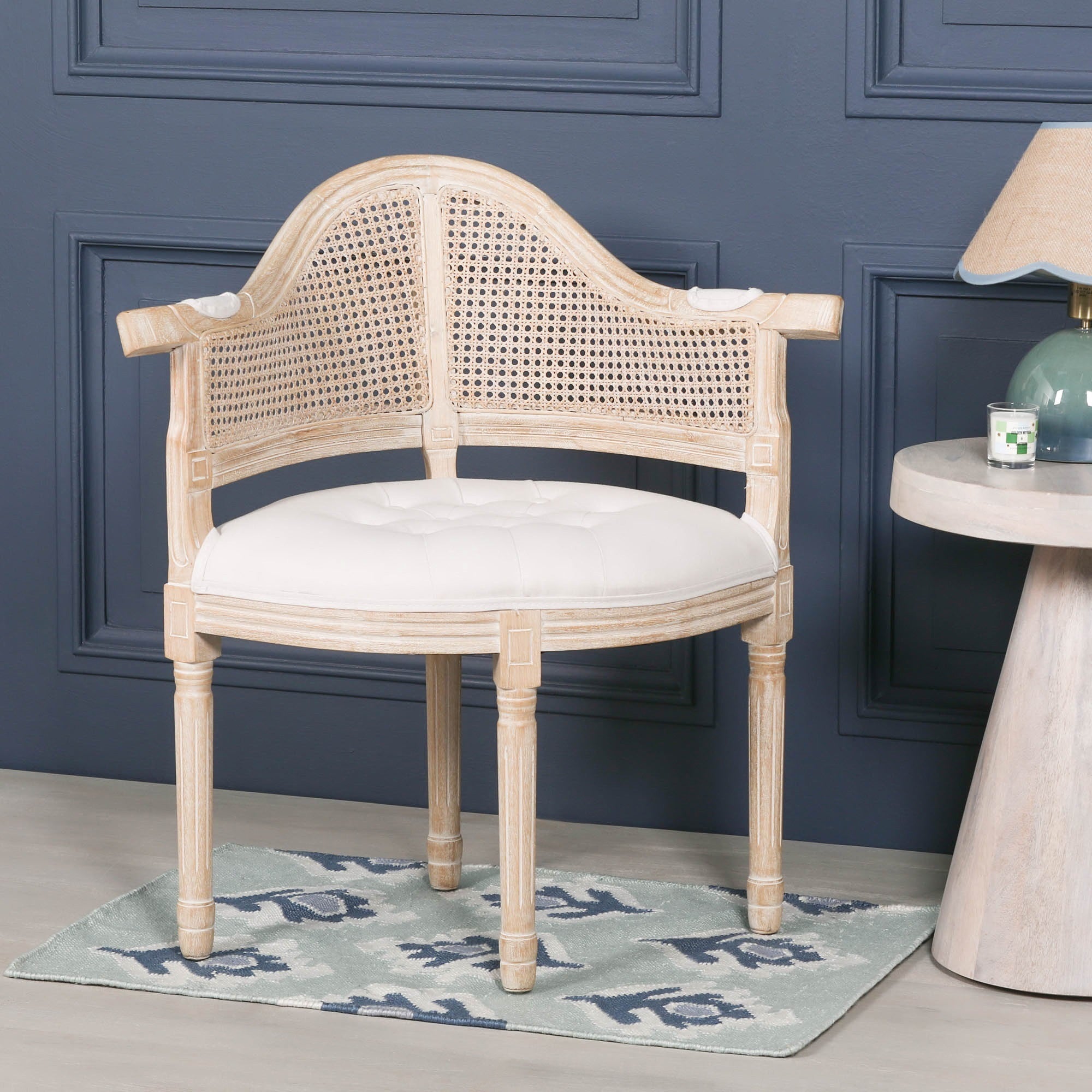 Lucienne Louis corner chair with linen upholstery, woven cane backrest and washed wood frame styled beside a side table in a sophisticated living room setting.