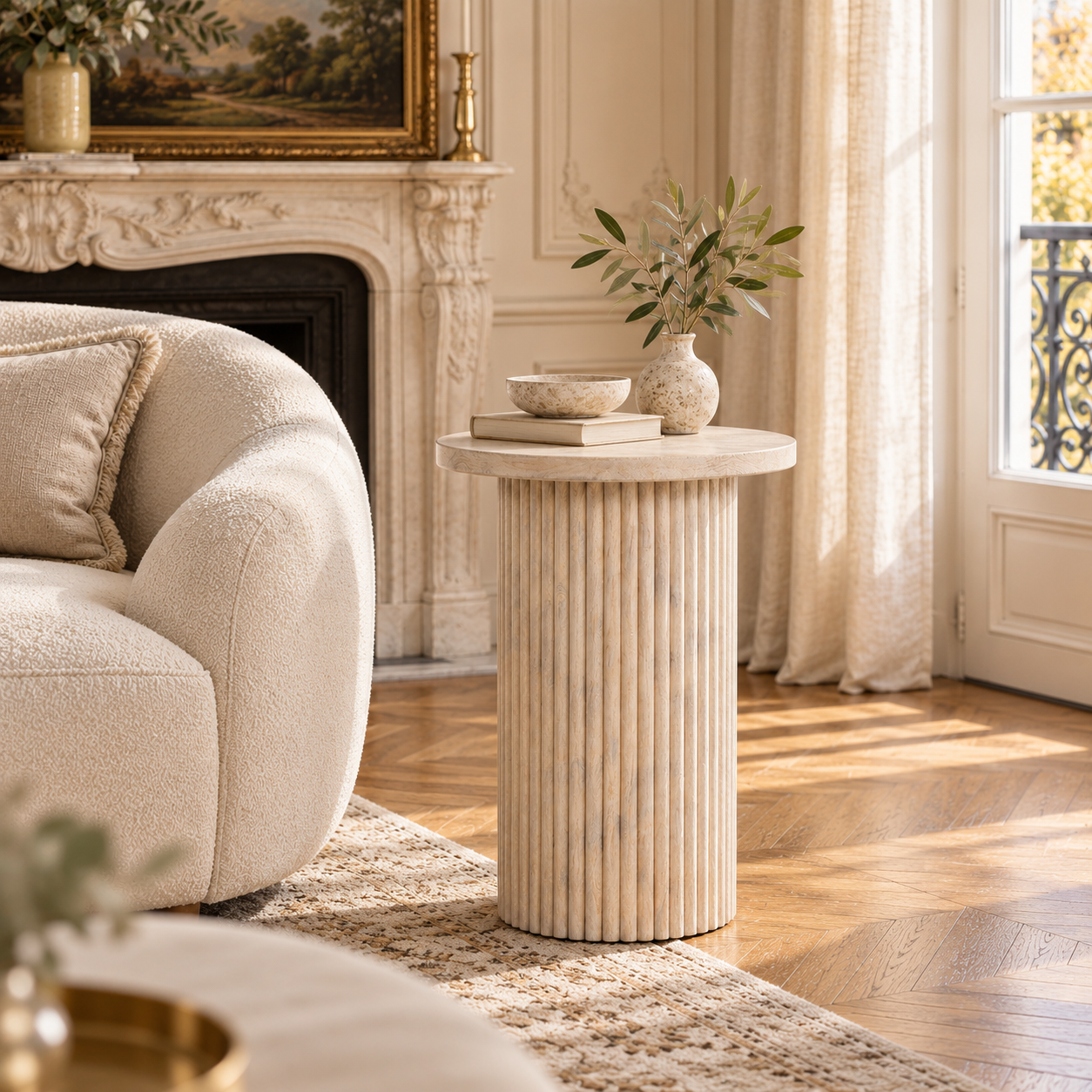 Margaux washed mango wood round side table with ribbed base in a bright living room with cream chair, fireplace and rug.