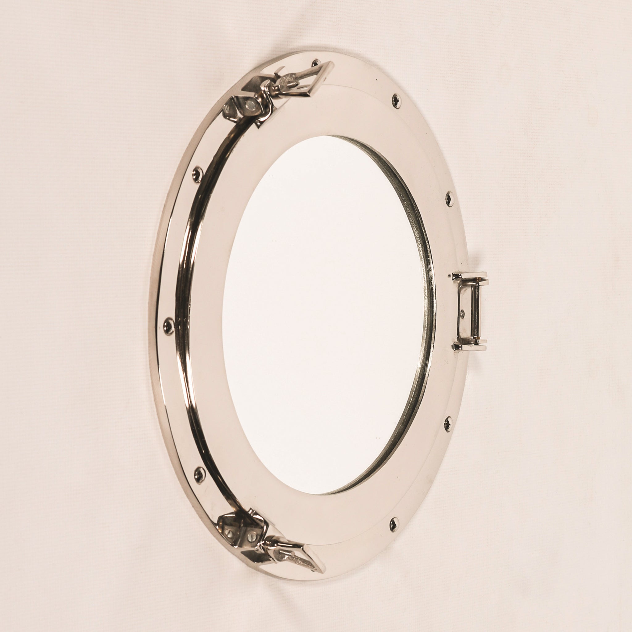 Angled view of the Marin extra-large round porthole wall mirror, highlighting its polished aluminium metal frame, circular mirror, rivet detailing, side hinge and nautical clasps.