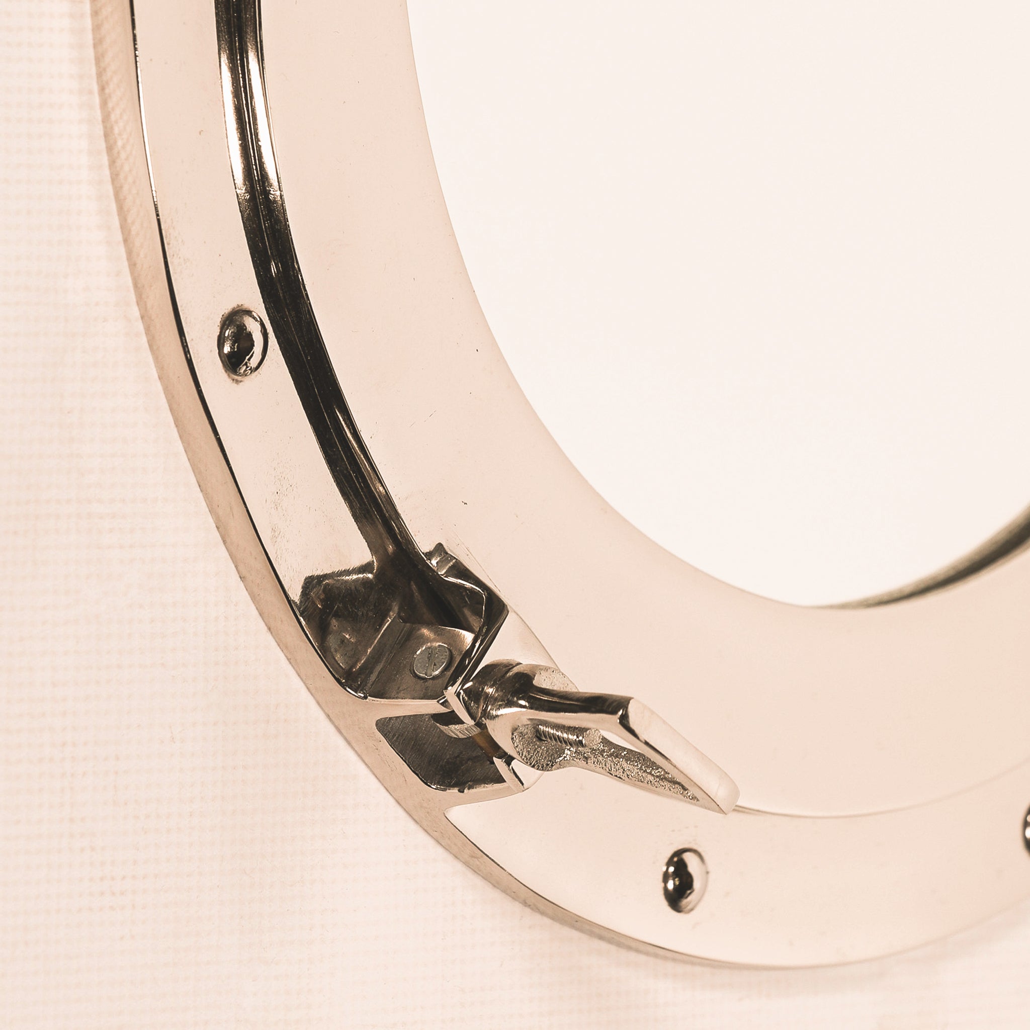 Close-up of the Marin round porthole wall mirror showing the polished aluminium frame, reflective metal finish, recessed rivet detail and traditional nautical locking clasp.