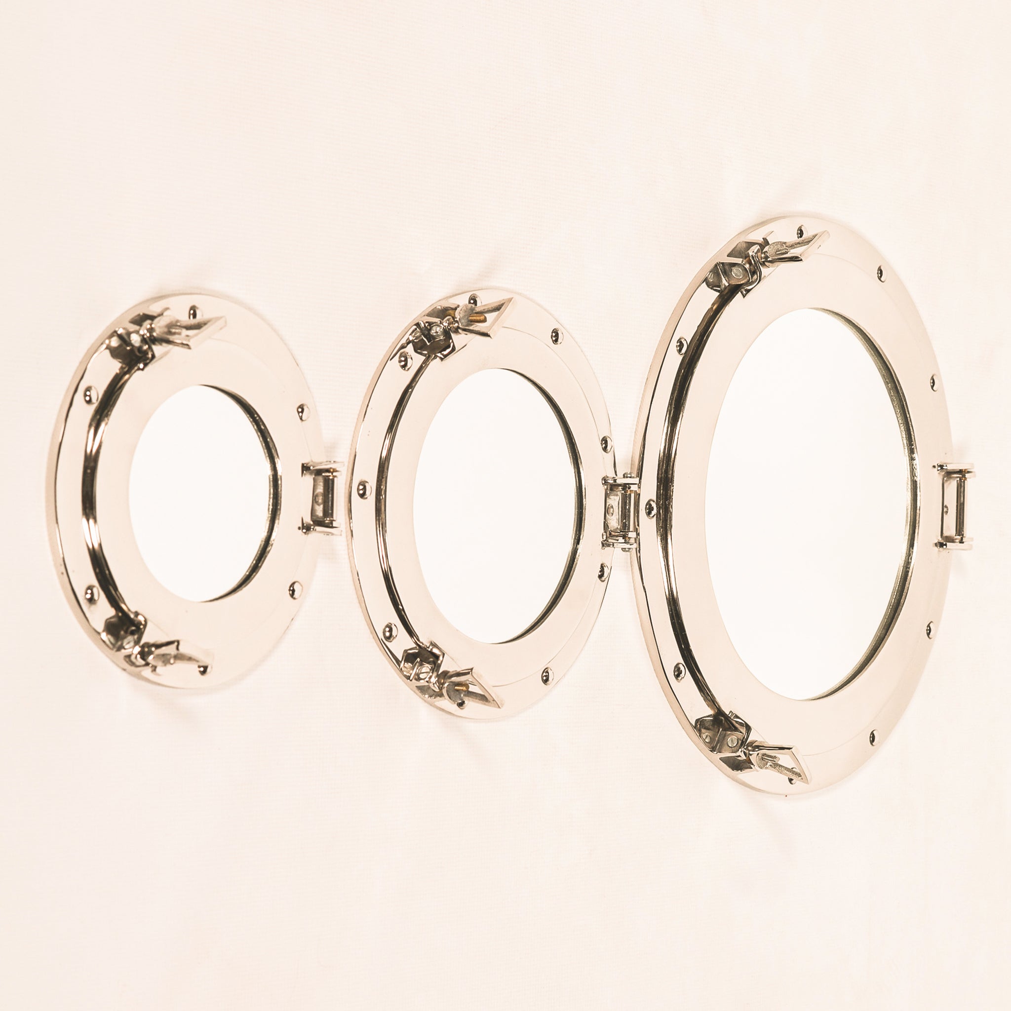 Three Marin round porthole wall mirrors in different sizes, showing polished aluminium frames with nautical rivet detailing, hinged sides and decorative locking clasps.