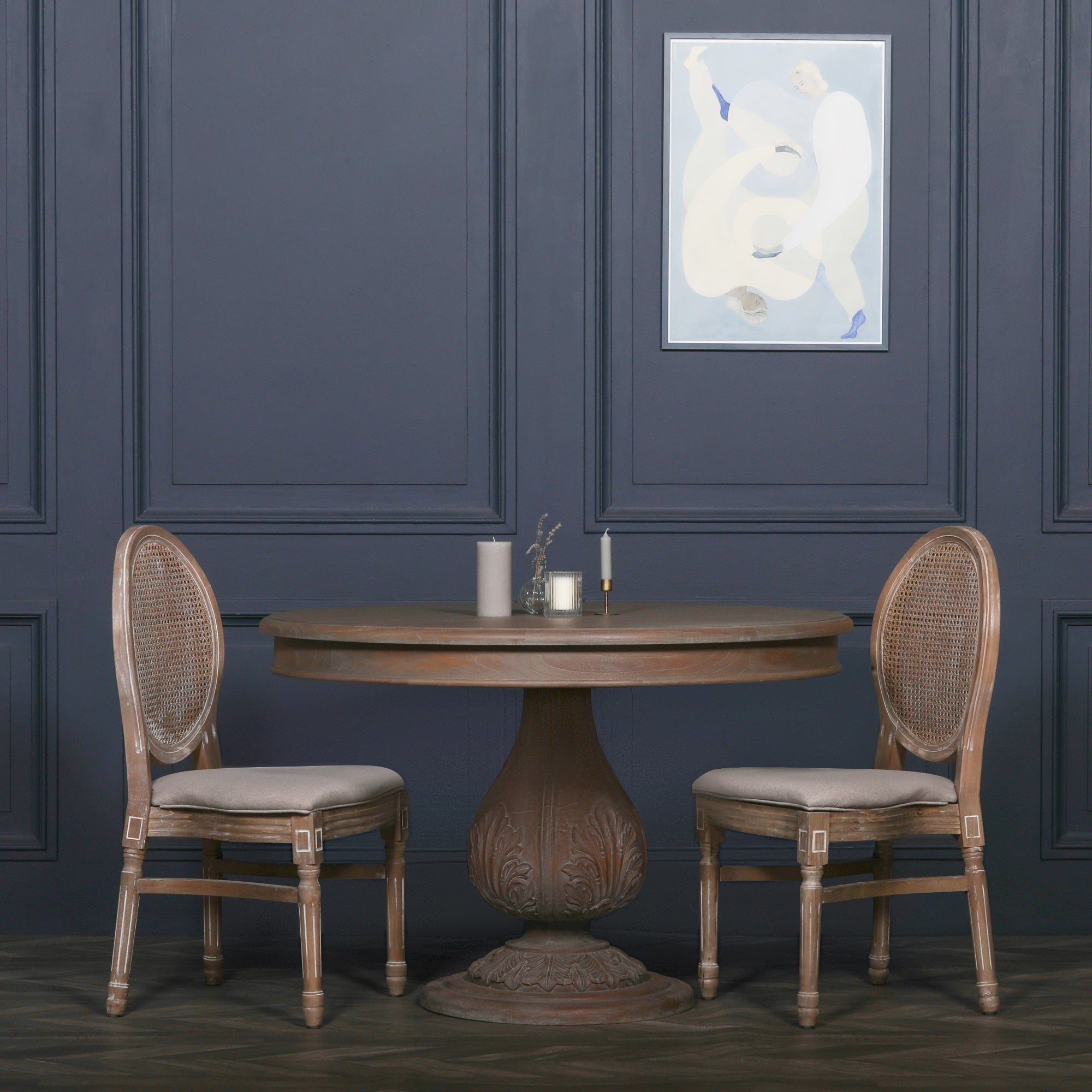 Mathis round pedestal dining table in reclaimed cedar wood styled with Louis dining chairs against a dark panelled wall.