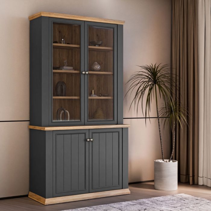 Montclair tall grey and oak effect display cabinet with glazed doors, wooden display shelves and lower storage cupboards styled beside a plant in a living room.