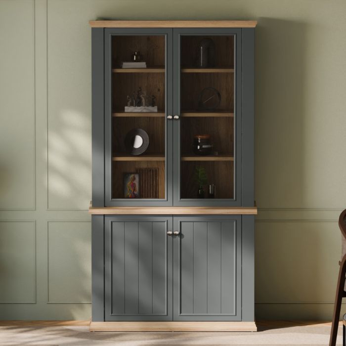 Montclair tall 4 door display cabinet in grey and oak effect with glazed upper doors, wooden shelving and lower storage cupboards styled in a living room.