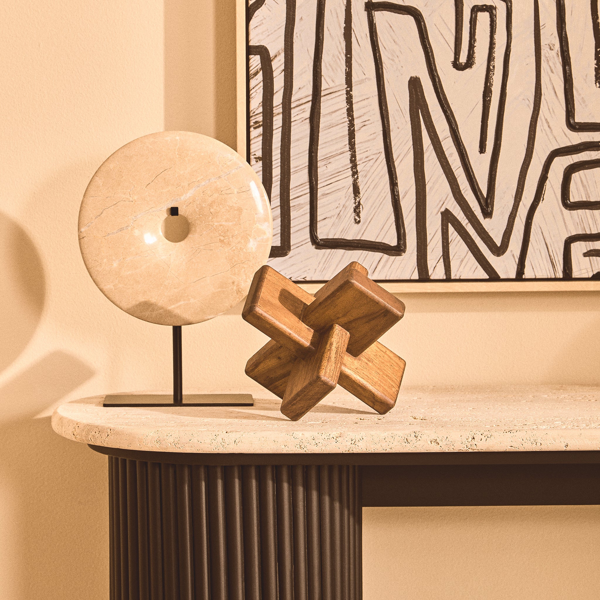 Noé acacia wood sculptural ornament displayed on a stone console table with a circular decorative object and monochrome abstract artwork