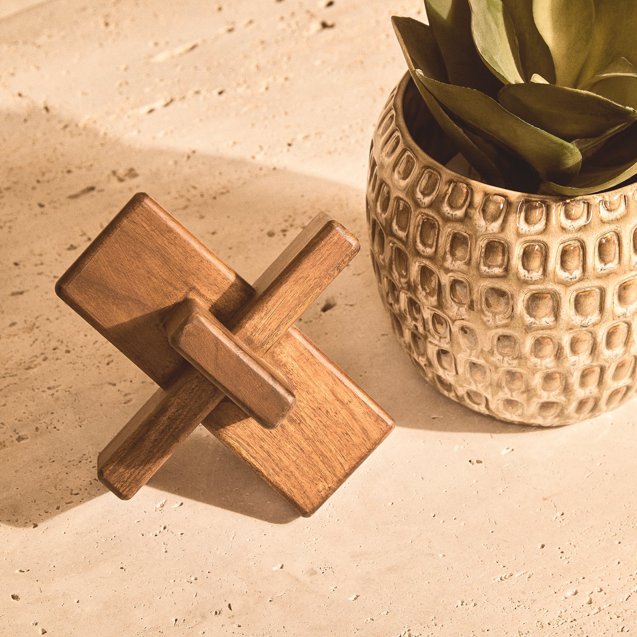 Noé brown acacia wood sculptural object beside a textured ceramic planter on a stone tabletop, showing its geometric interlocking design