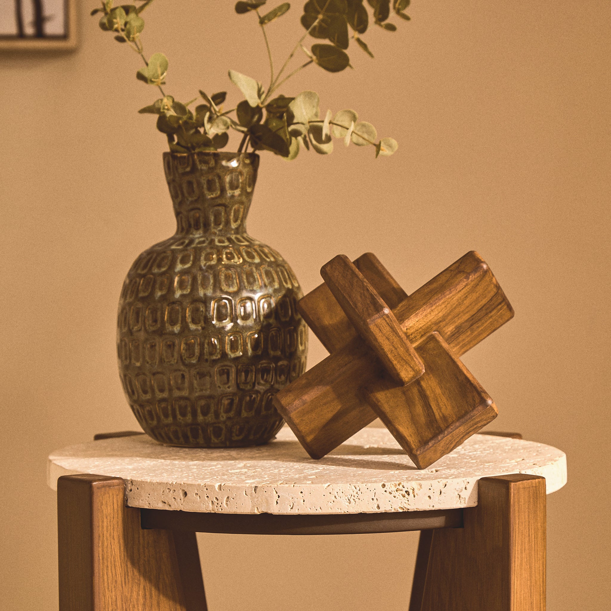 Noé hand-carved brown acacia wood sculpture styled beside a textured vase with foliage on a round stone-topped side table
