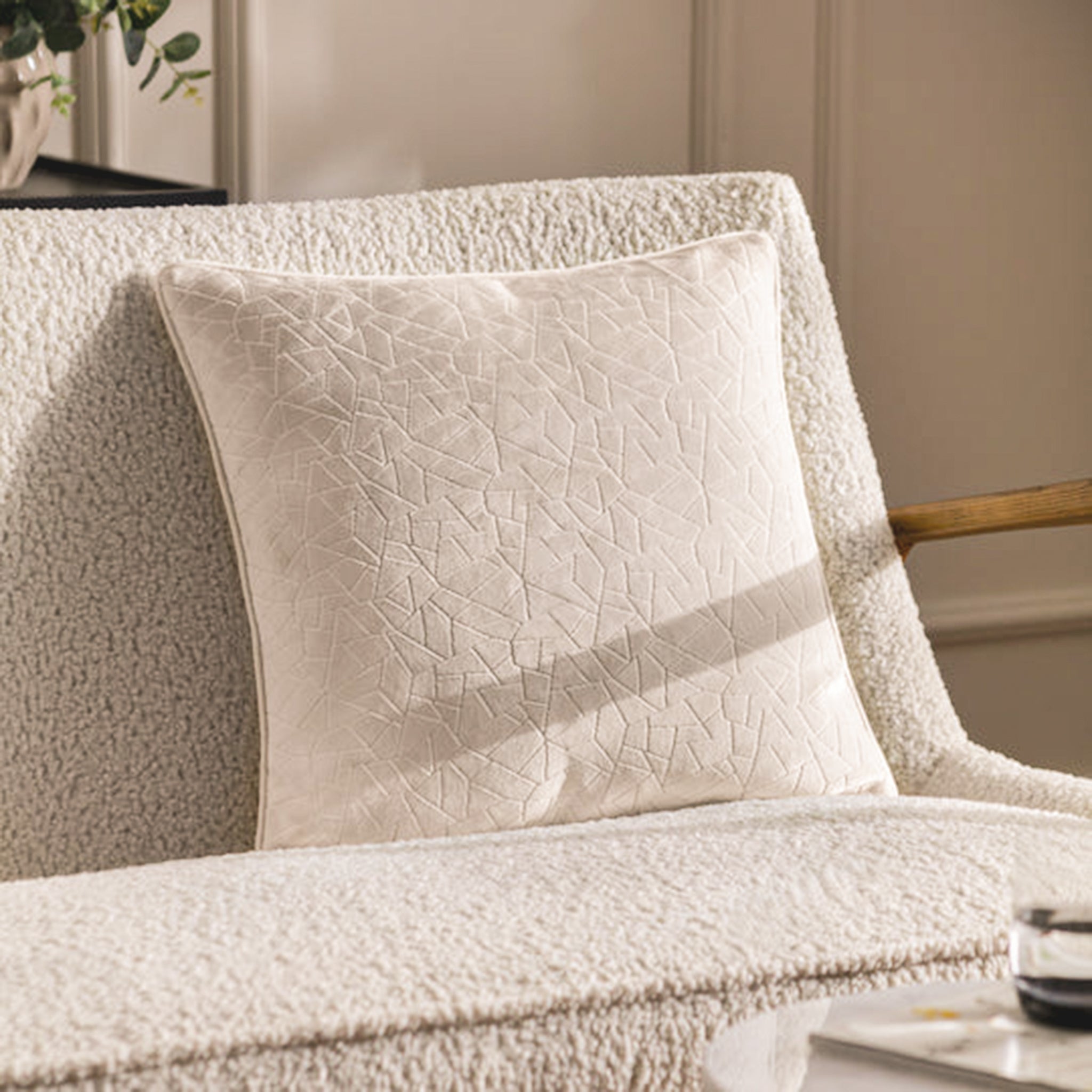 Noé Maëva soft milk cream cut velvet cushion styled on a cream bouclé sofa, showcasing its subtle geometric texture, plush square form and piped edging in an elegant neutral interior.