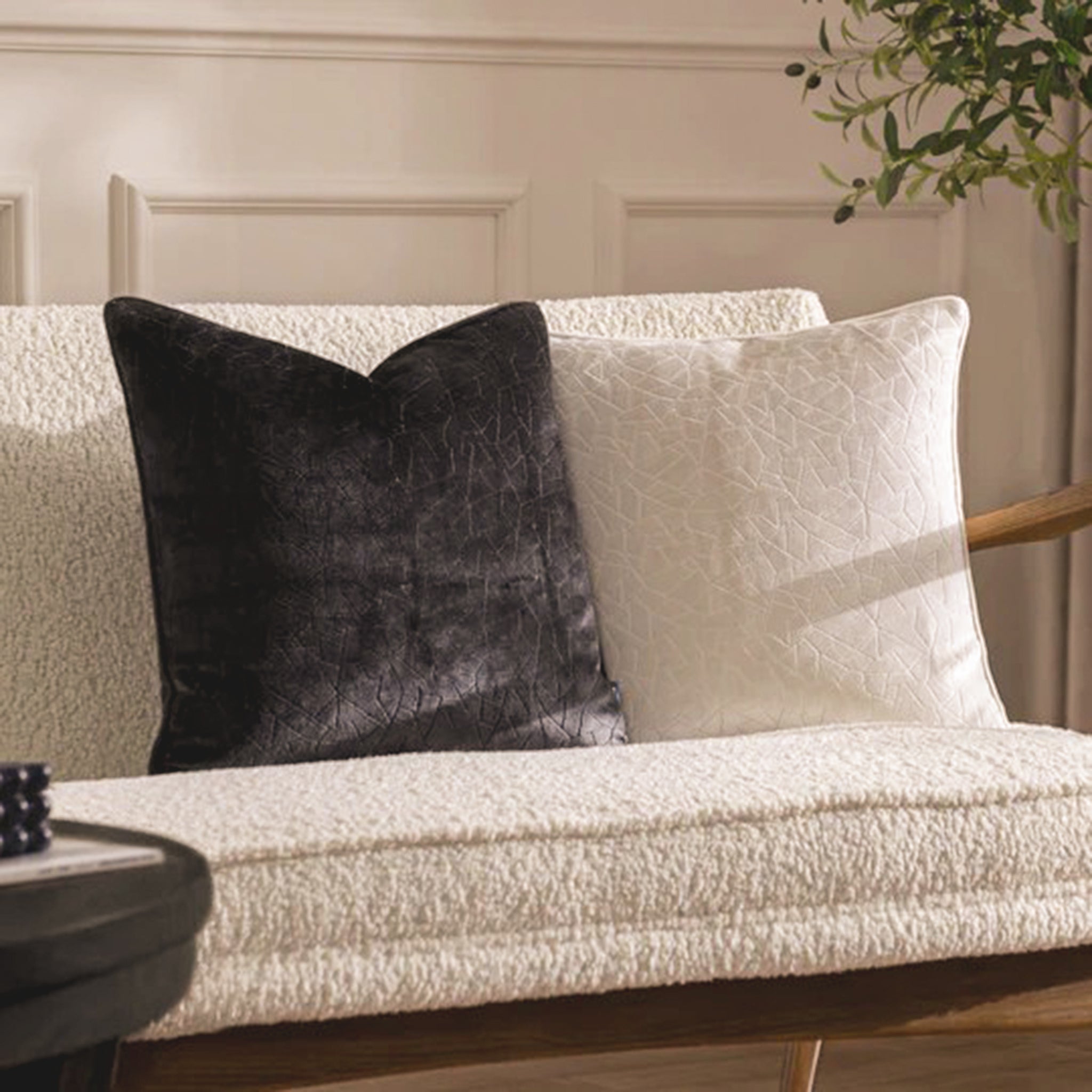 Noé Maëva soft milk cream cut velvet cushion styled on a textured cream sofa beside a contrasting dark cushion, showing its elegant geometric pattern and piped edging in a neutral living room.