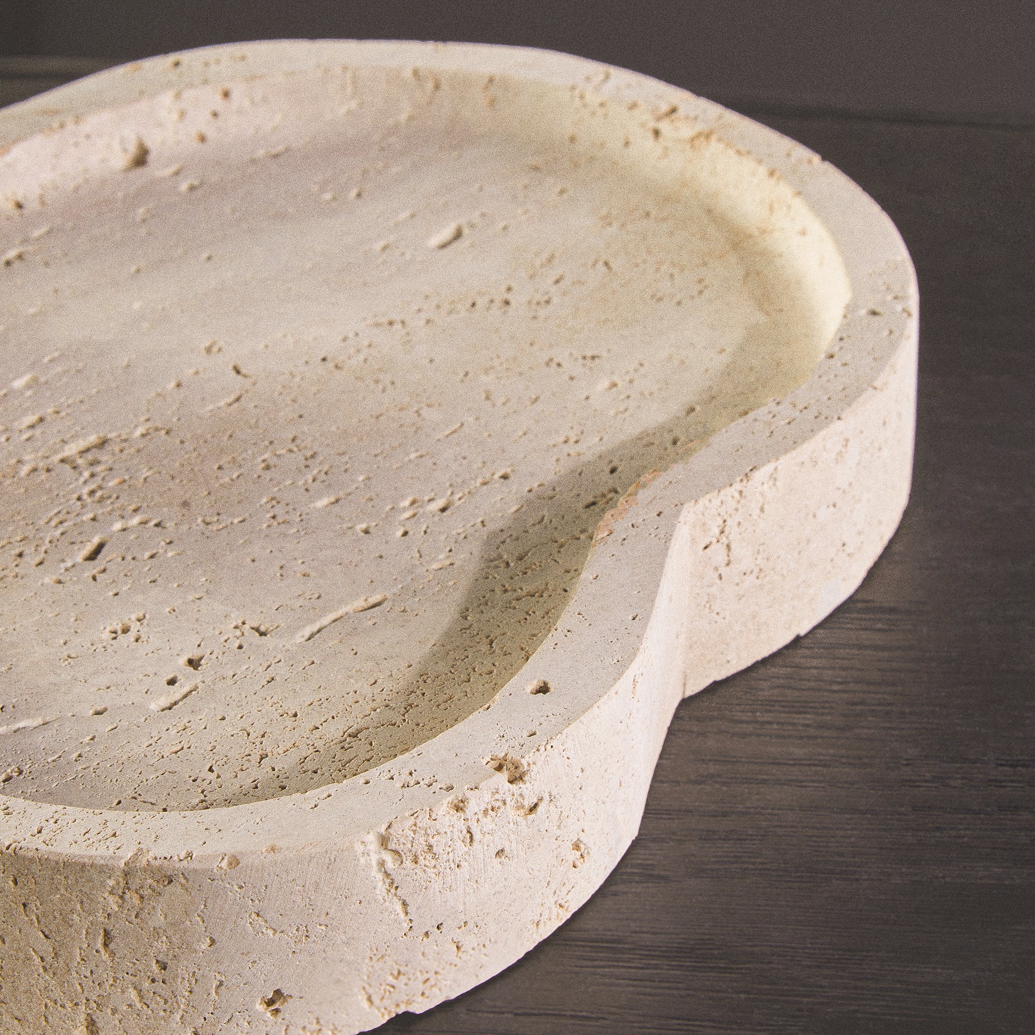 Detailed close-up of the Noé Travertine Tray highlighting its organic curved form, recessed surface and distinctive porous natural travertine texture.