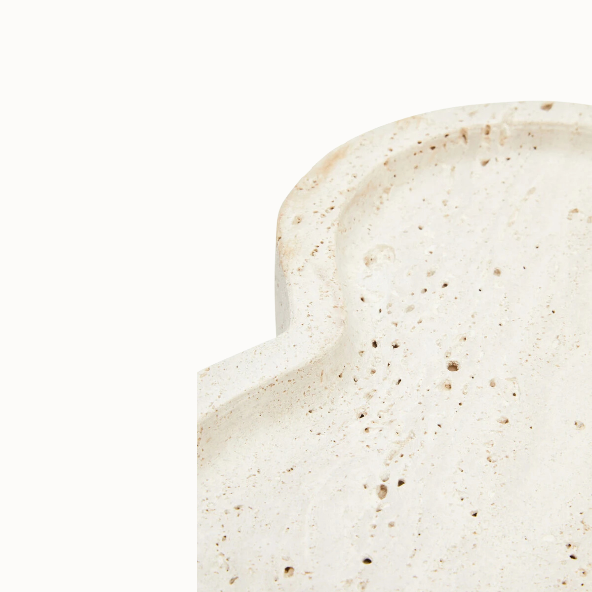 Close-up of Noé irregular travertine tray rim showing curved form, natural pores and beige stone on white.