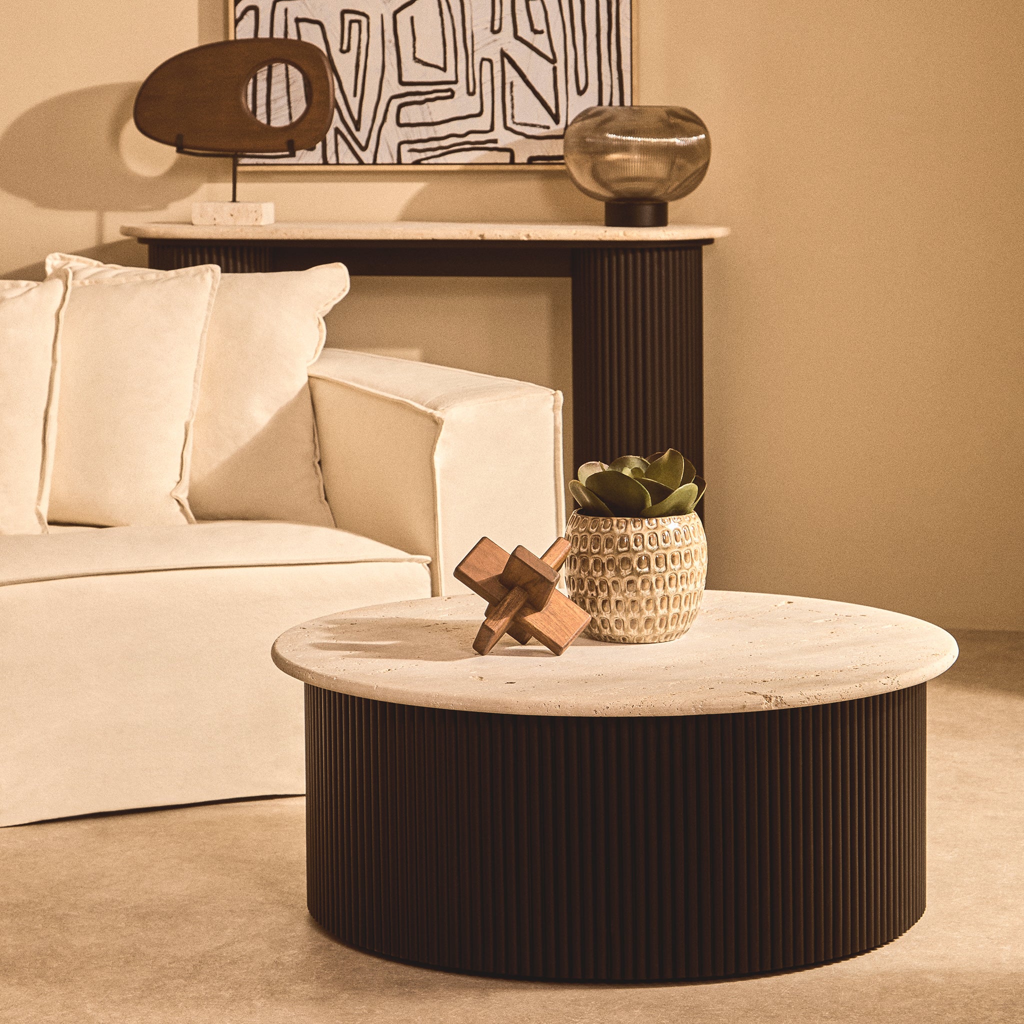 Noé hand-carved acacia wood sculptural object styled with a ceramic planter on a round stone coffee table in a contemporary living room