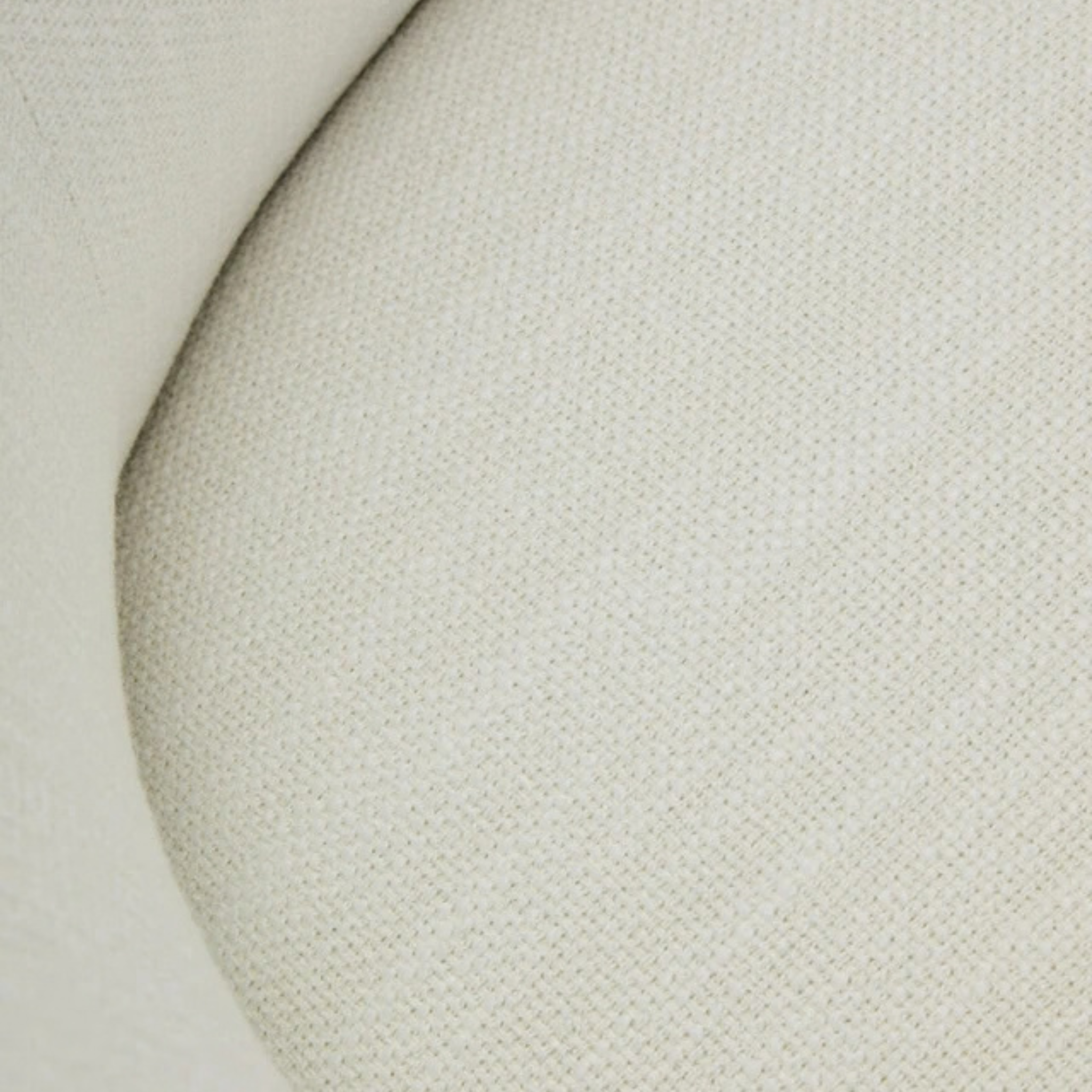 Close-up of Odile armchair textured cream woven upholstery and curved seam detailing filling the background