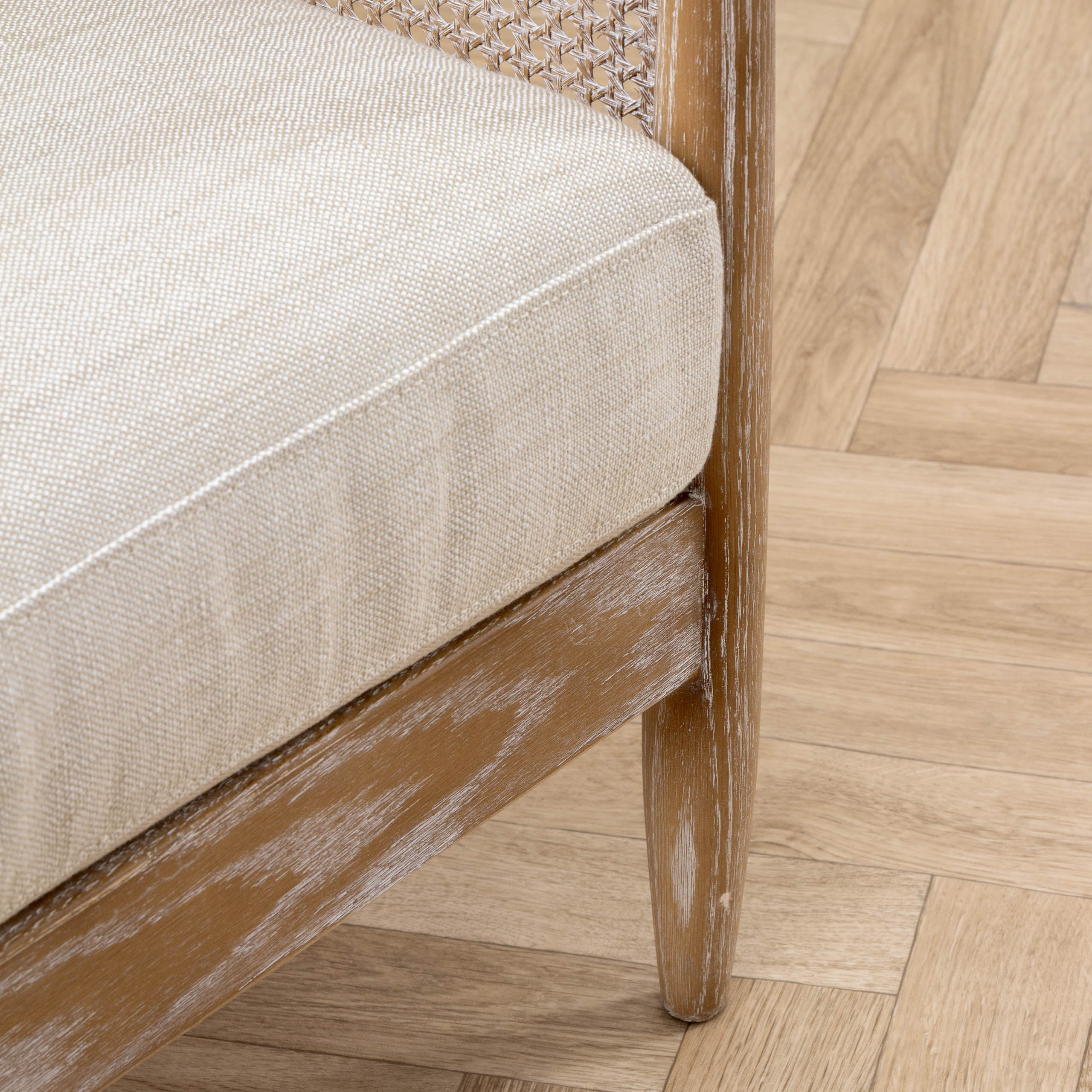 Close-up of Remi linen chair showing cream woven upholstery and warm wood frame on herringbone flooring.