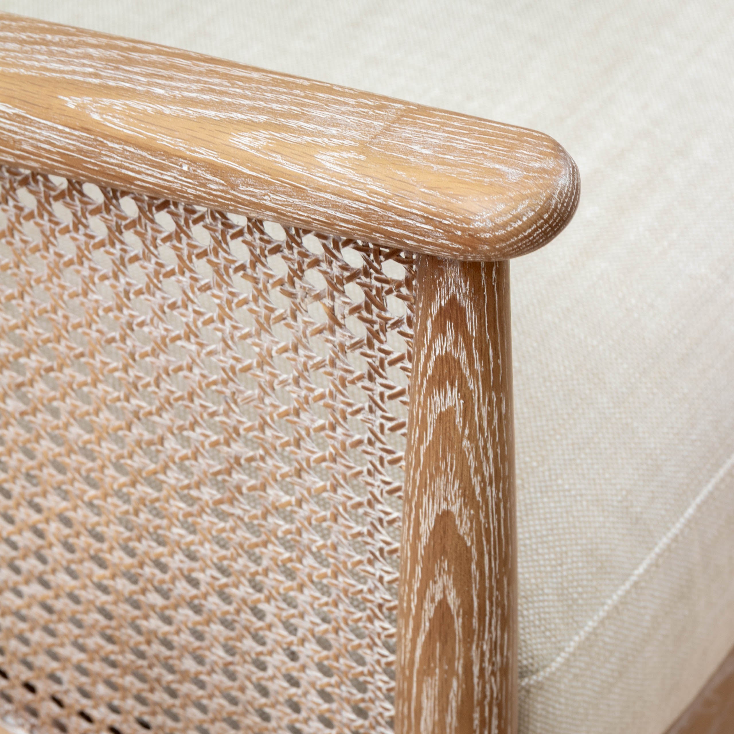 Close-up of Remi rattan 2-seater chair showing woven cane side, warm wood frame and cream linen upholstery.