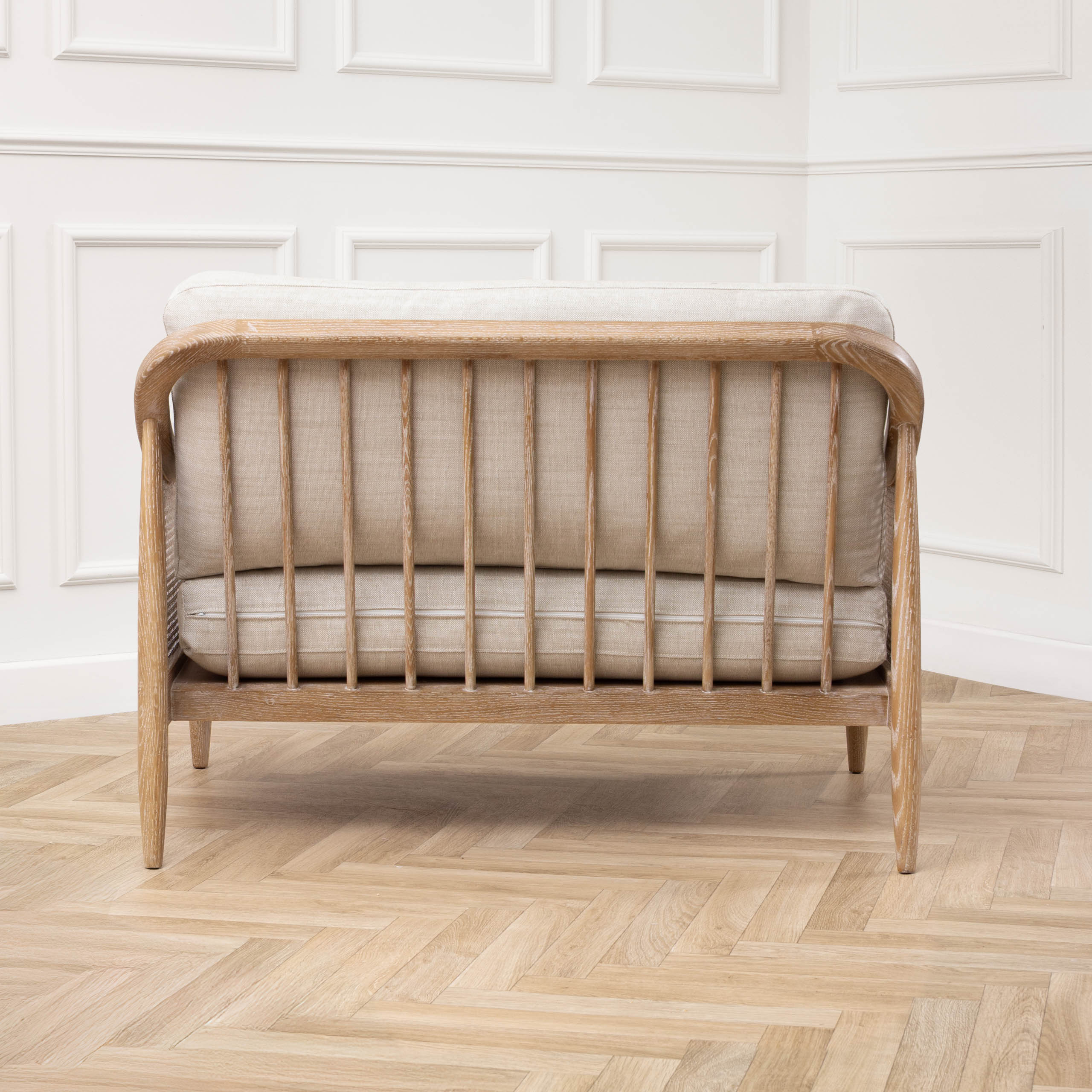 Rear view of Remi rattan 2-seater chair with linen cushions against white panelled walls and wood flooring.