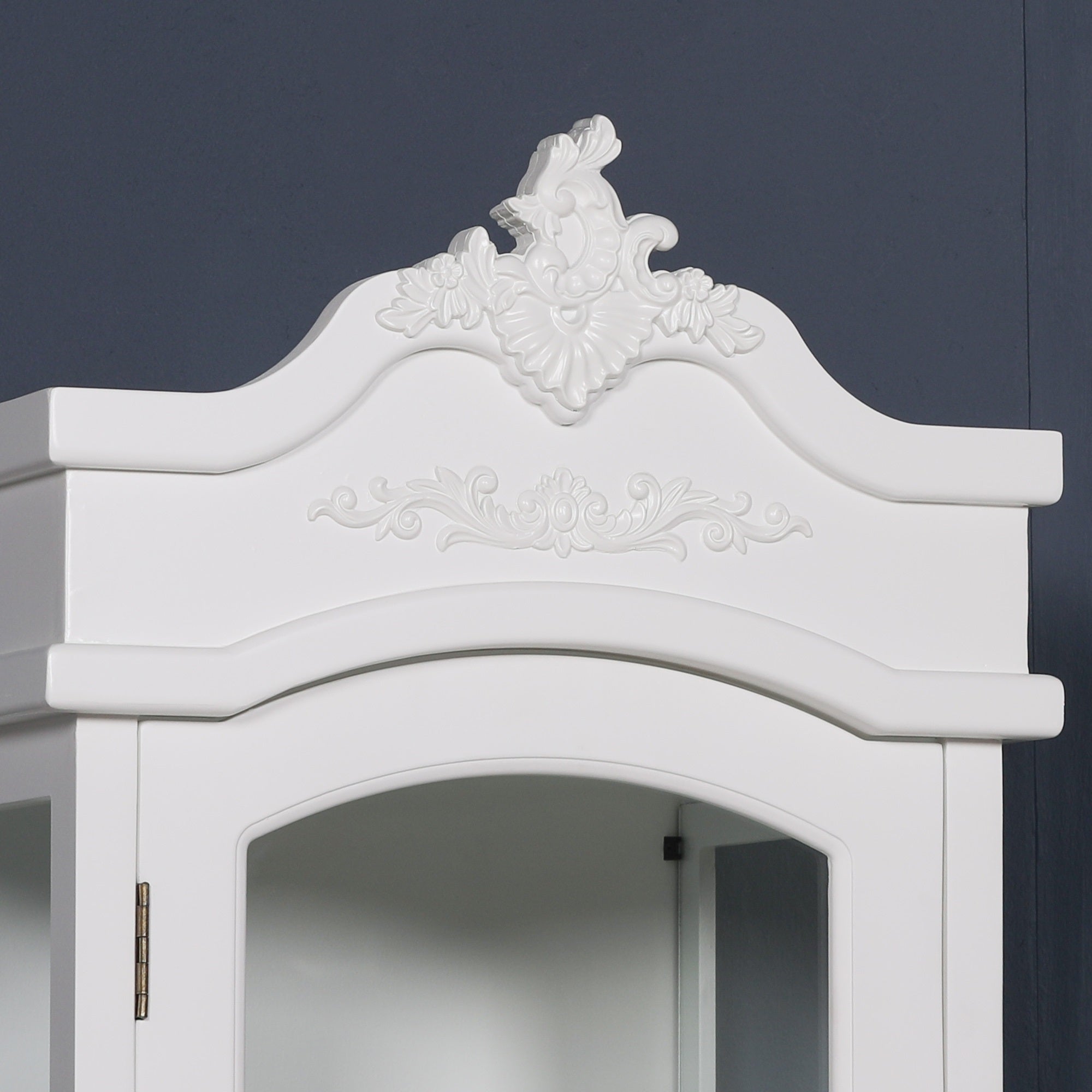 Close-up of the ornate carved crown and decorative cornice on the Rosalie Tall French Glass Display Cabinet with Drawer in Antique White, showcasing elegant French-inspired craftsmanship and antique-style detailing.